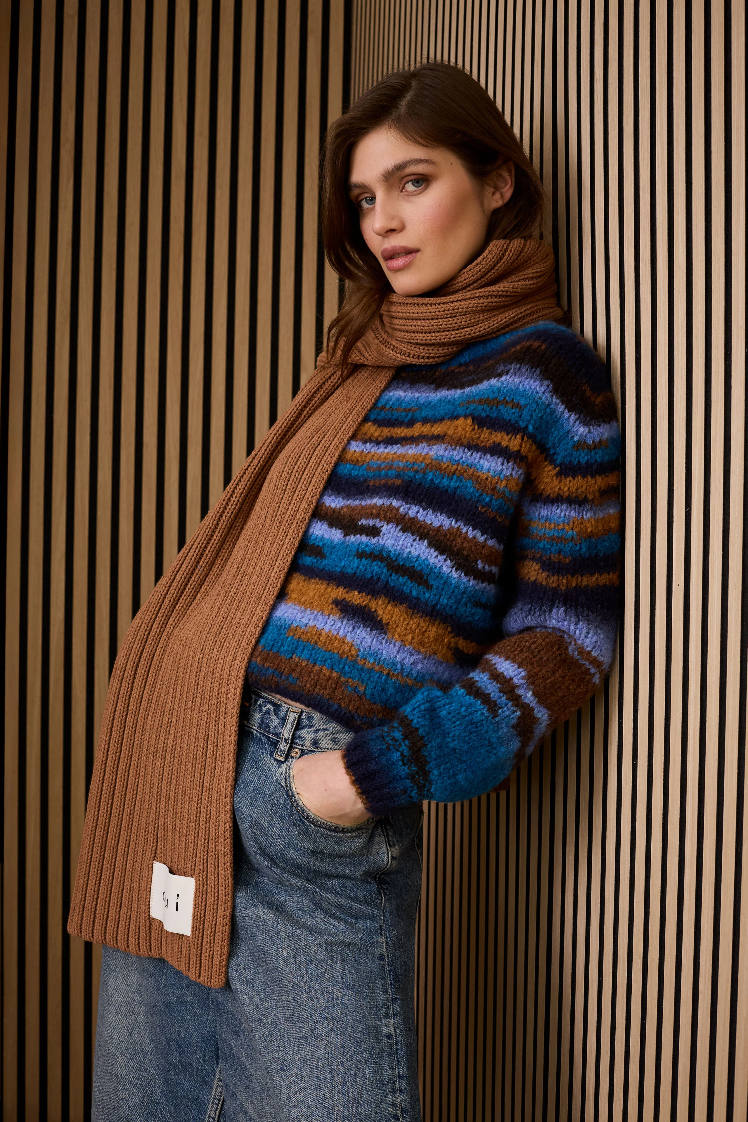 Damen-Schal in warmen Farben, kombiniert mit einem bunten Pullover und lässiger Jeans.
