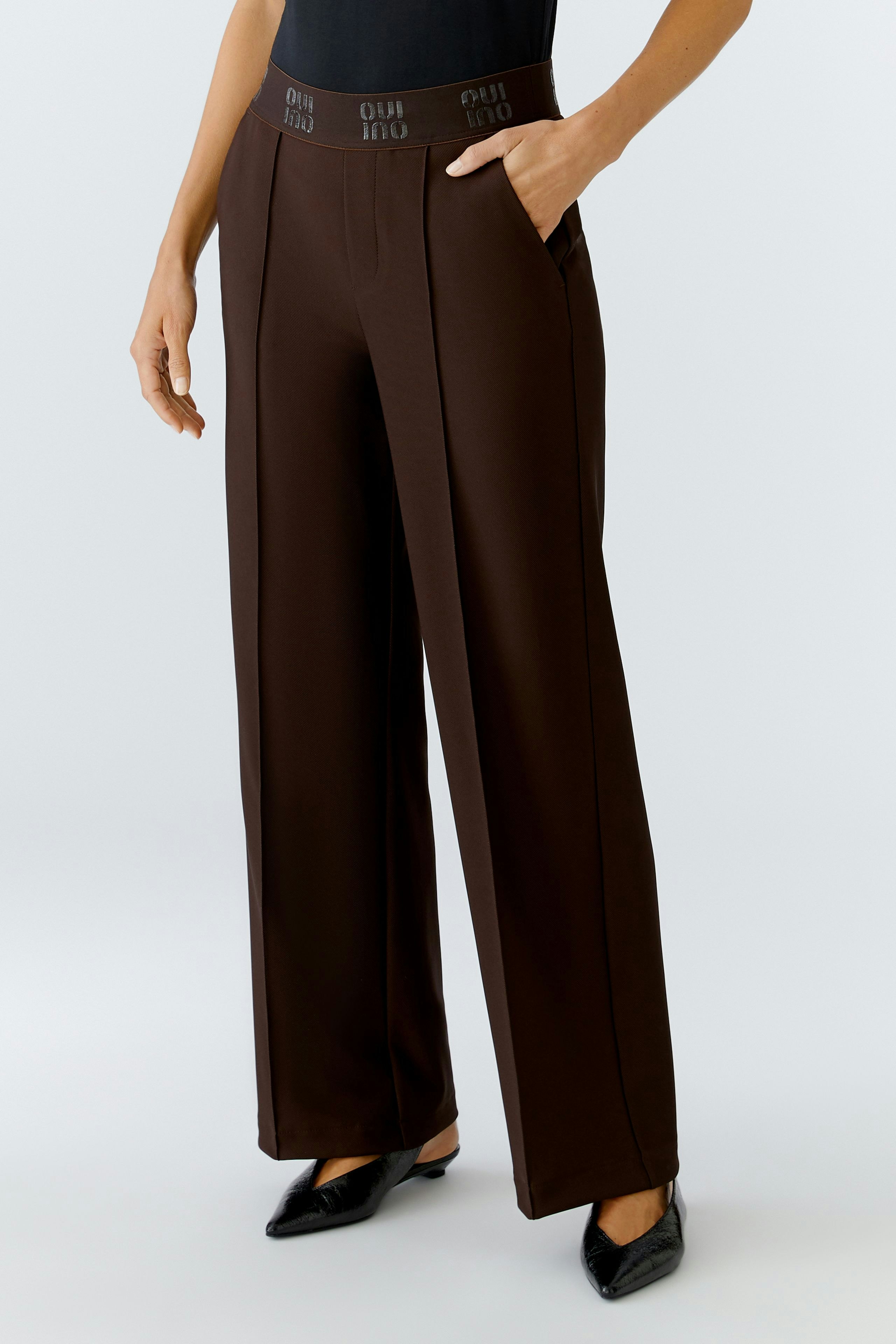 Modern women's trousers: A woman in brown wide-leg trousers with a logo waistband stands confidently.