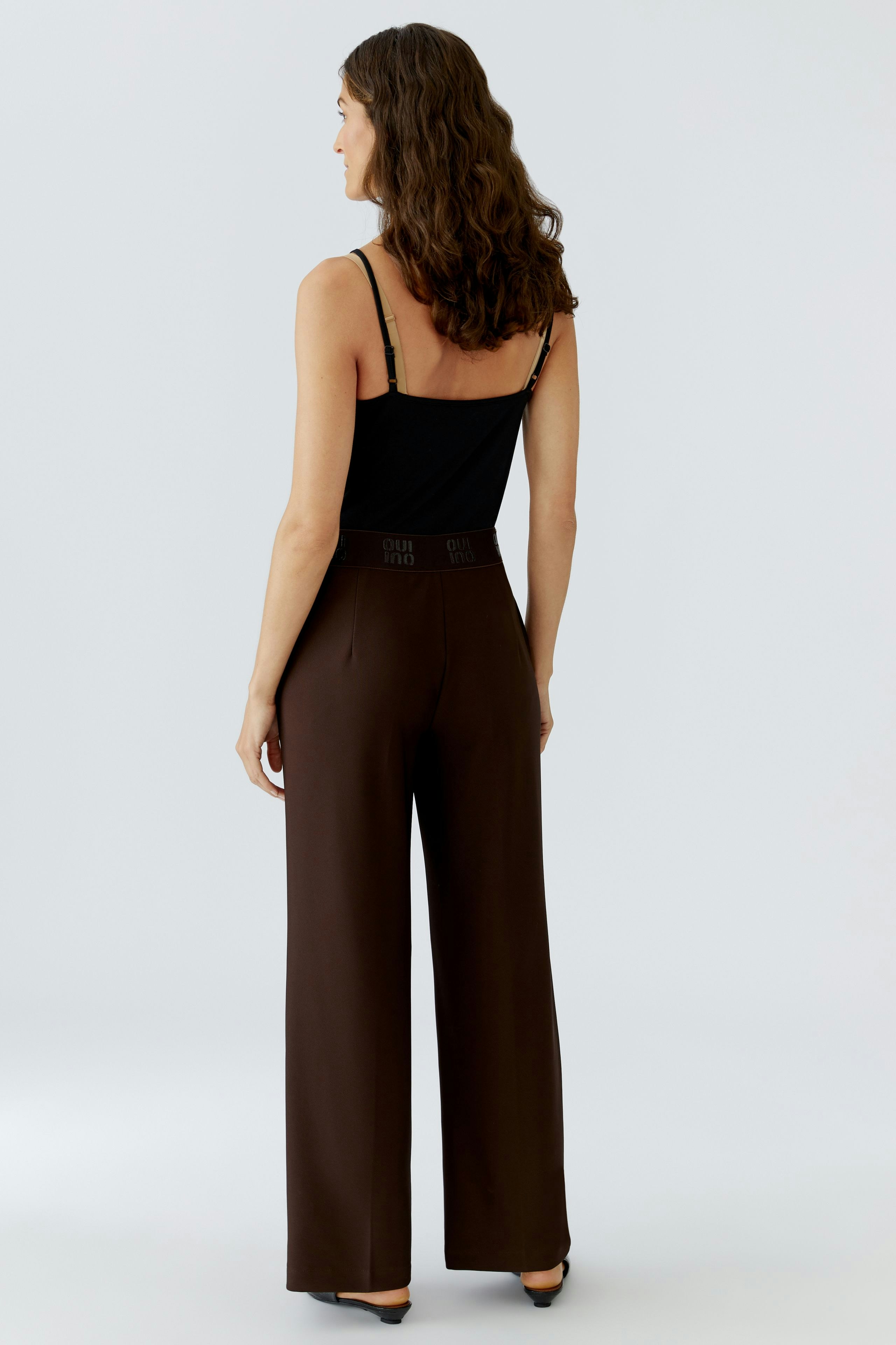 Stylish women's trousers: A woman in brown wide-leg trousers with a fitted waist, showcasing a modern look.