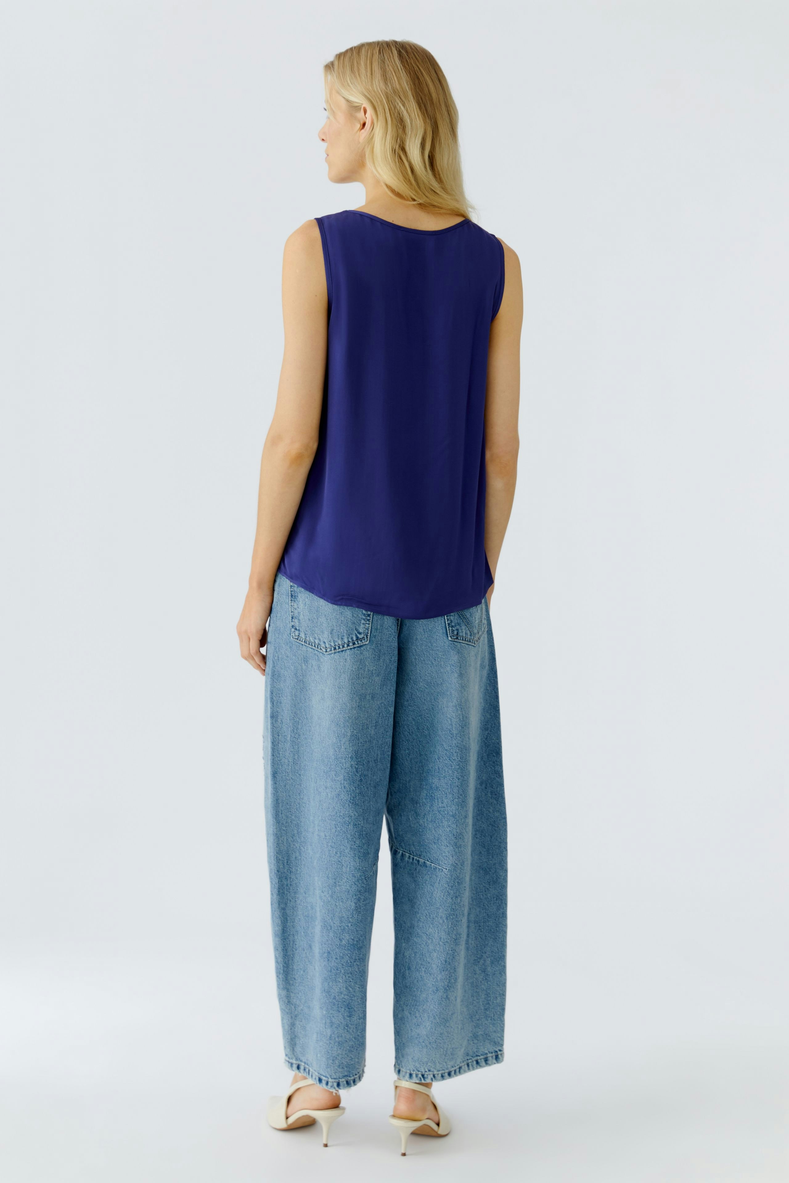 Casual women's top: A woman in a sleeveless navy top paired with loose denim pants.