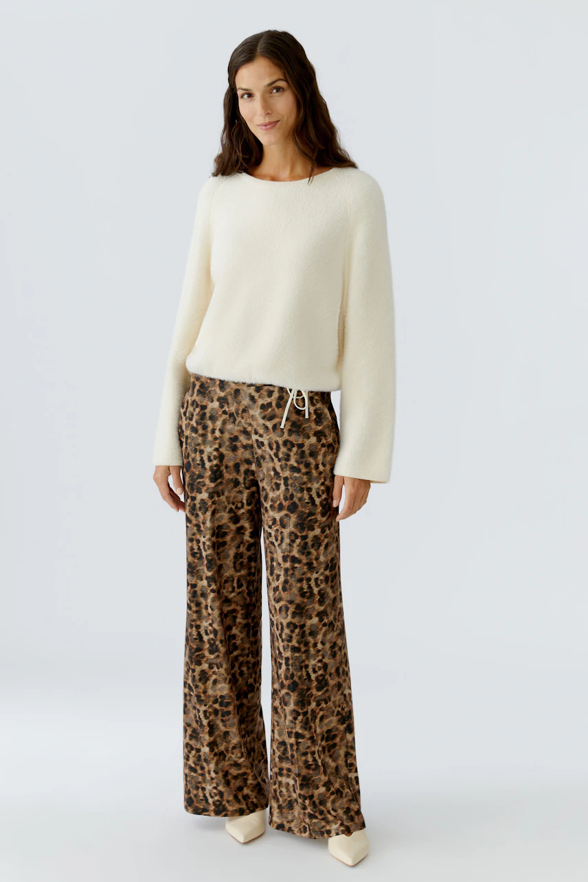 Bequeme Marlenehose: Frau trägt eine lässige Hose mit Leopardenmuster und einem weißen Pullover.