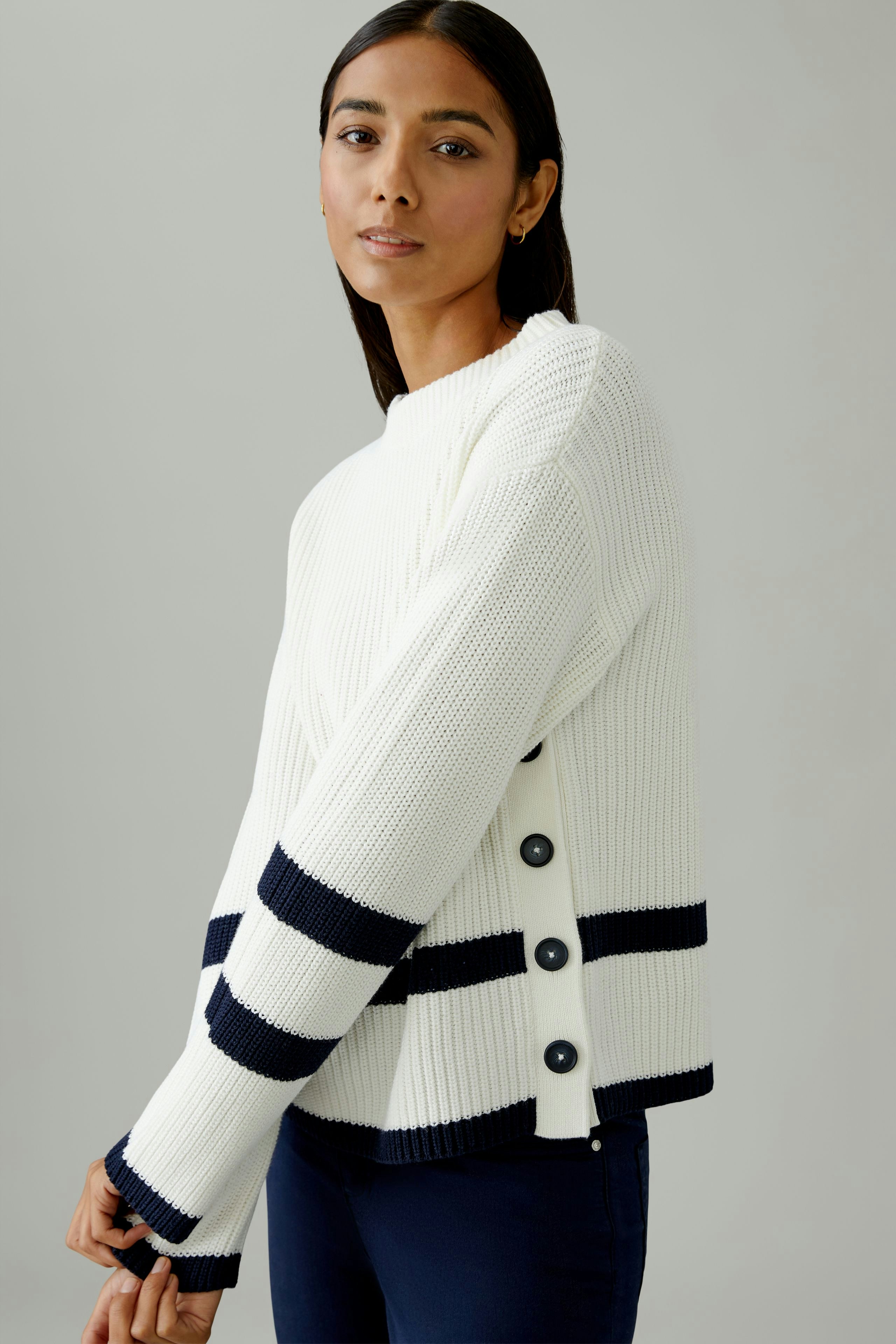 Casual women's pullover: Young woman in a white ribbed pullover with navy stripes and button details.