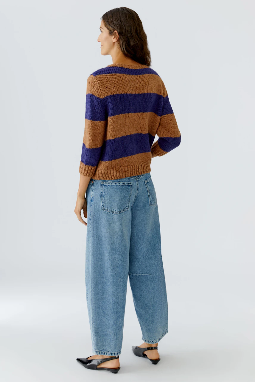 Casual women's pullover: A woman in a striped pullover with brown and purple hues, paired with loose jeans.