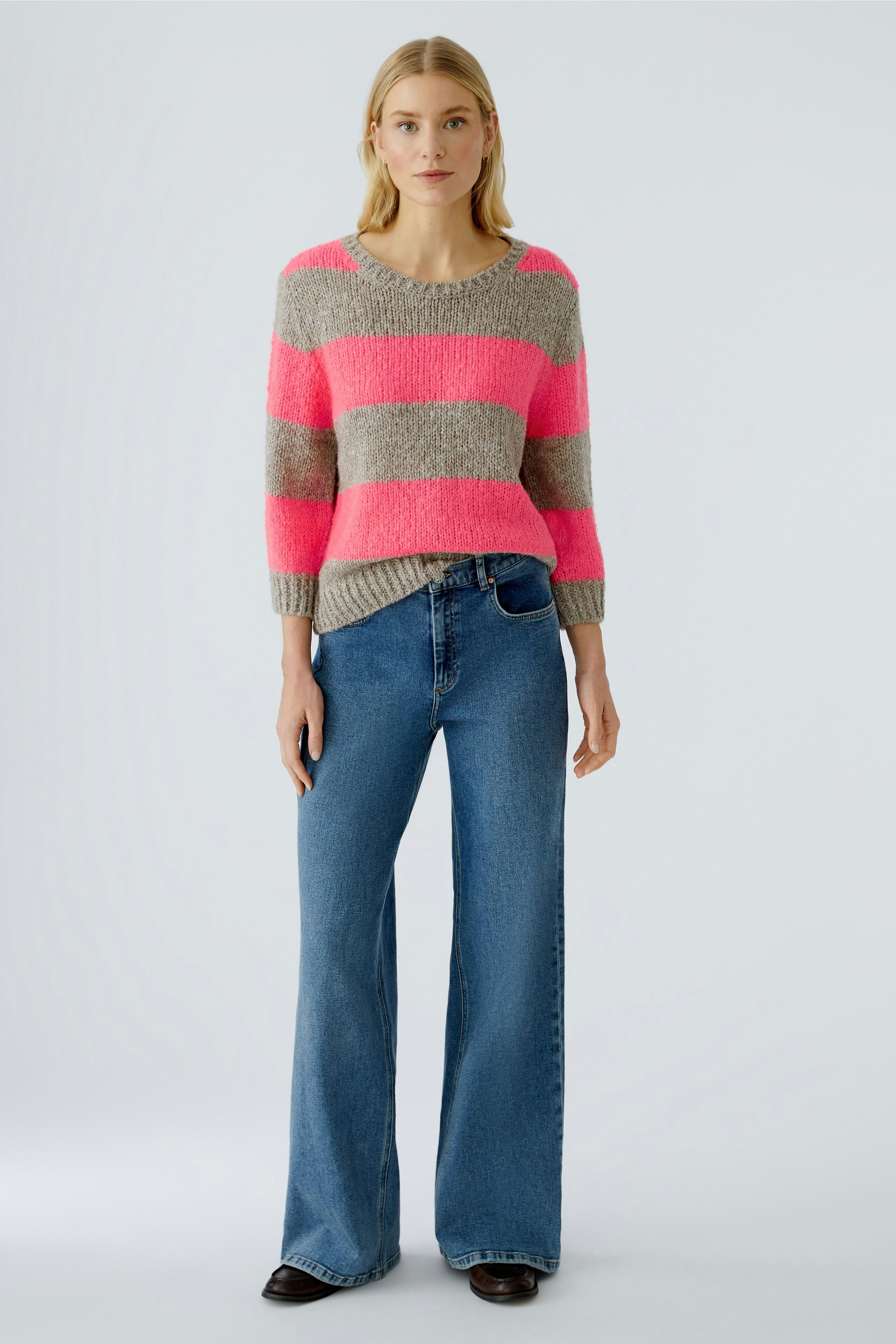 Casual women's pullover: A woman in a striped pullover with pink and gray hues, paired with wide-leg jeans.