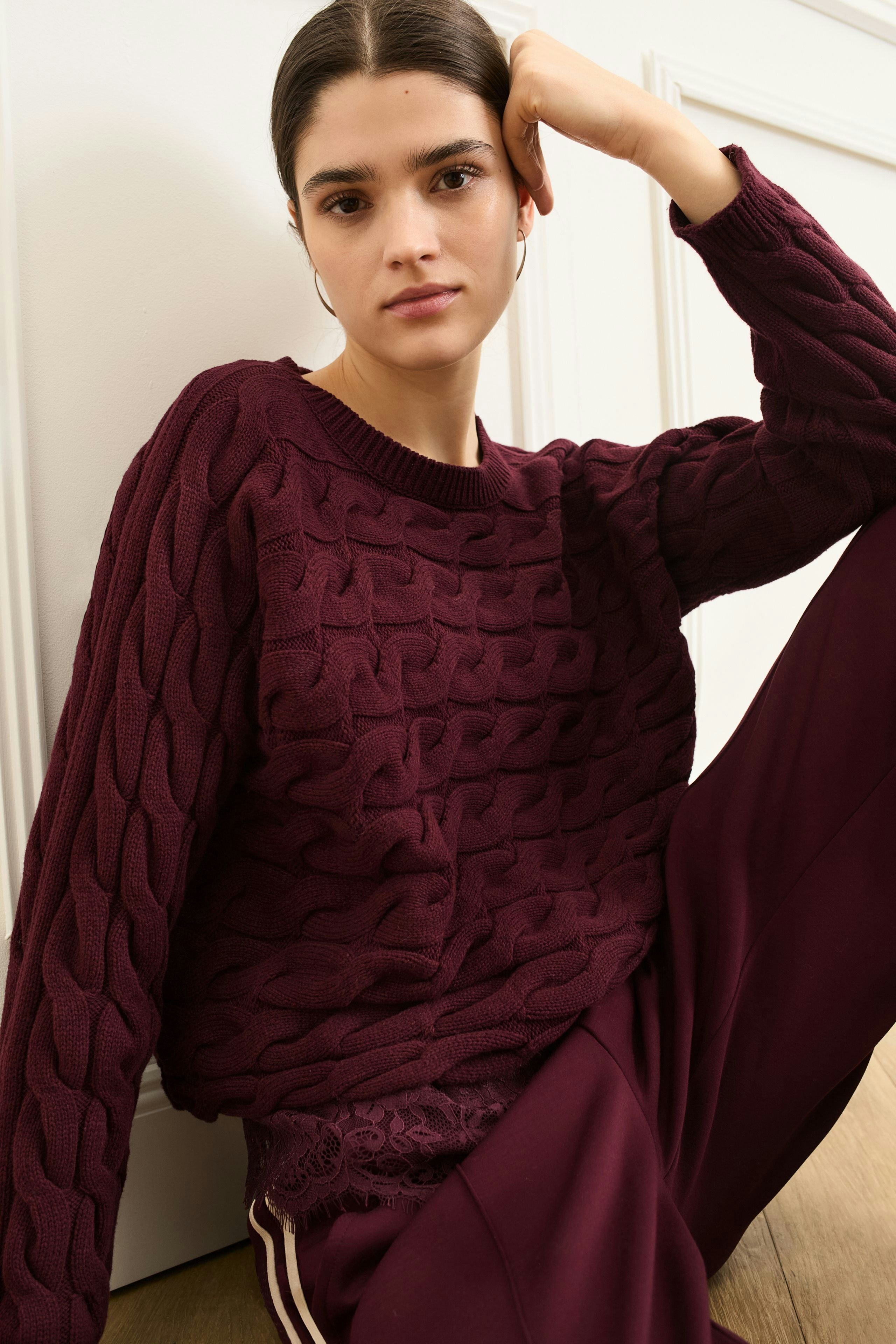 Casual women's pullover: Young woman in a burgundy cable-knit pullover, relaxed pose, stylish look.