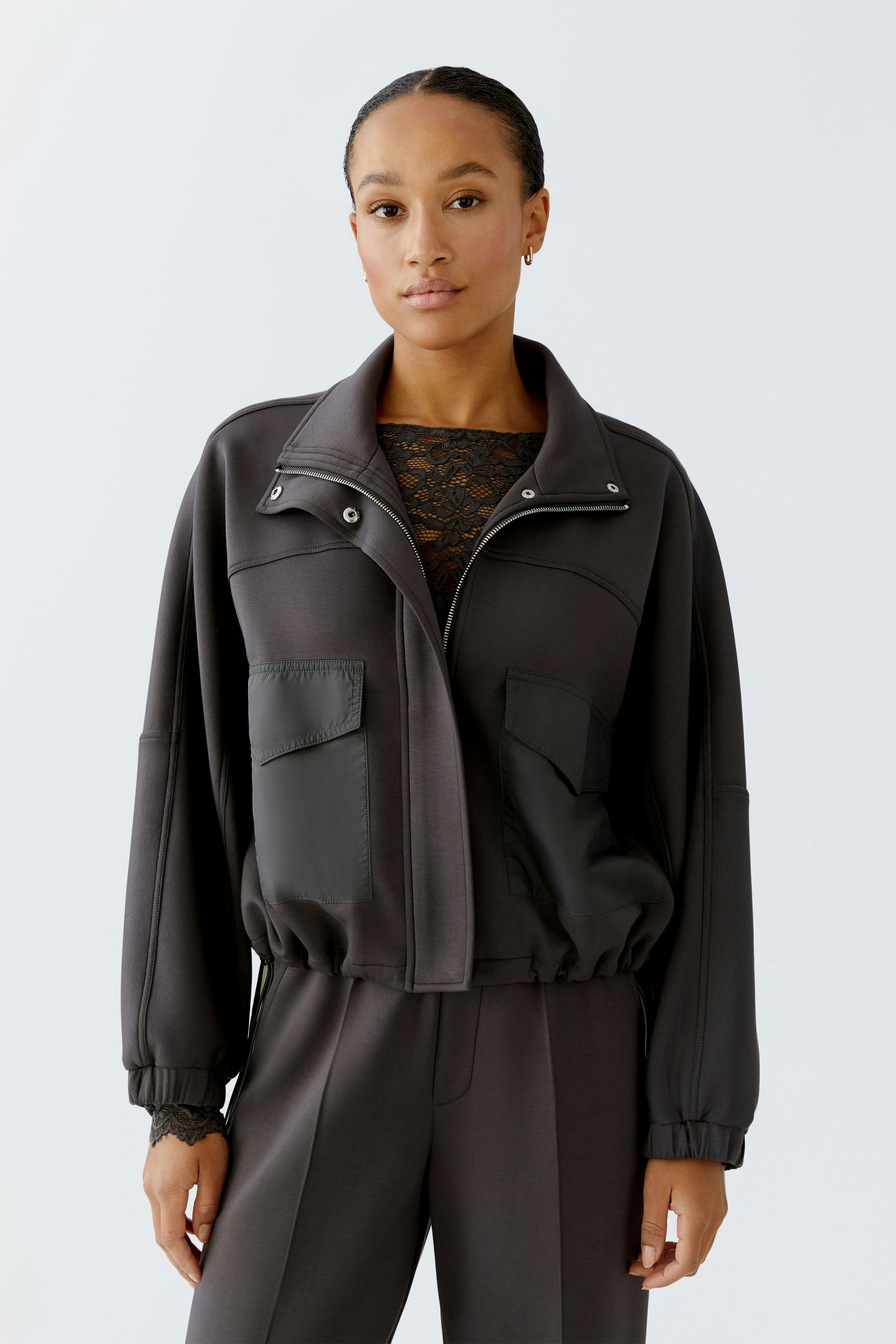 Casual women's jacket: A woman in a dark jacket with pockets, styled with a lace top and relaxed fit.