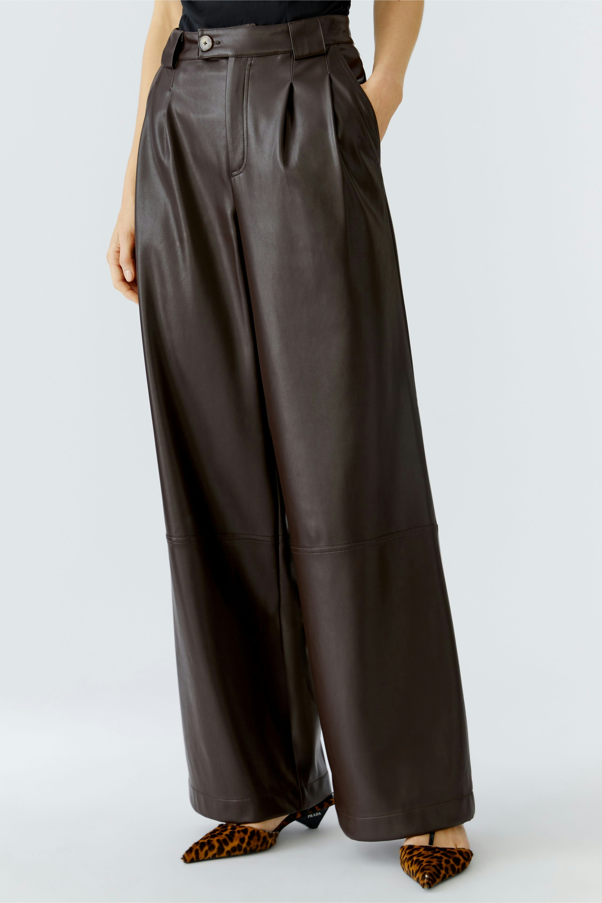Stylish women's pleated trousers in dark brown leather, paired with chic heels.