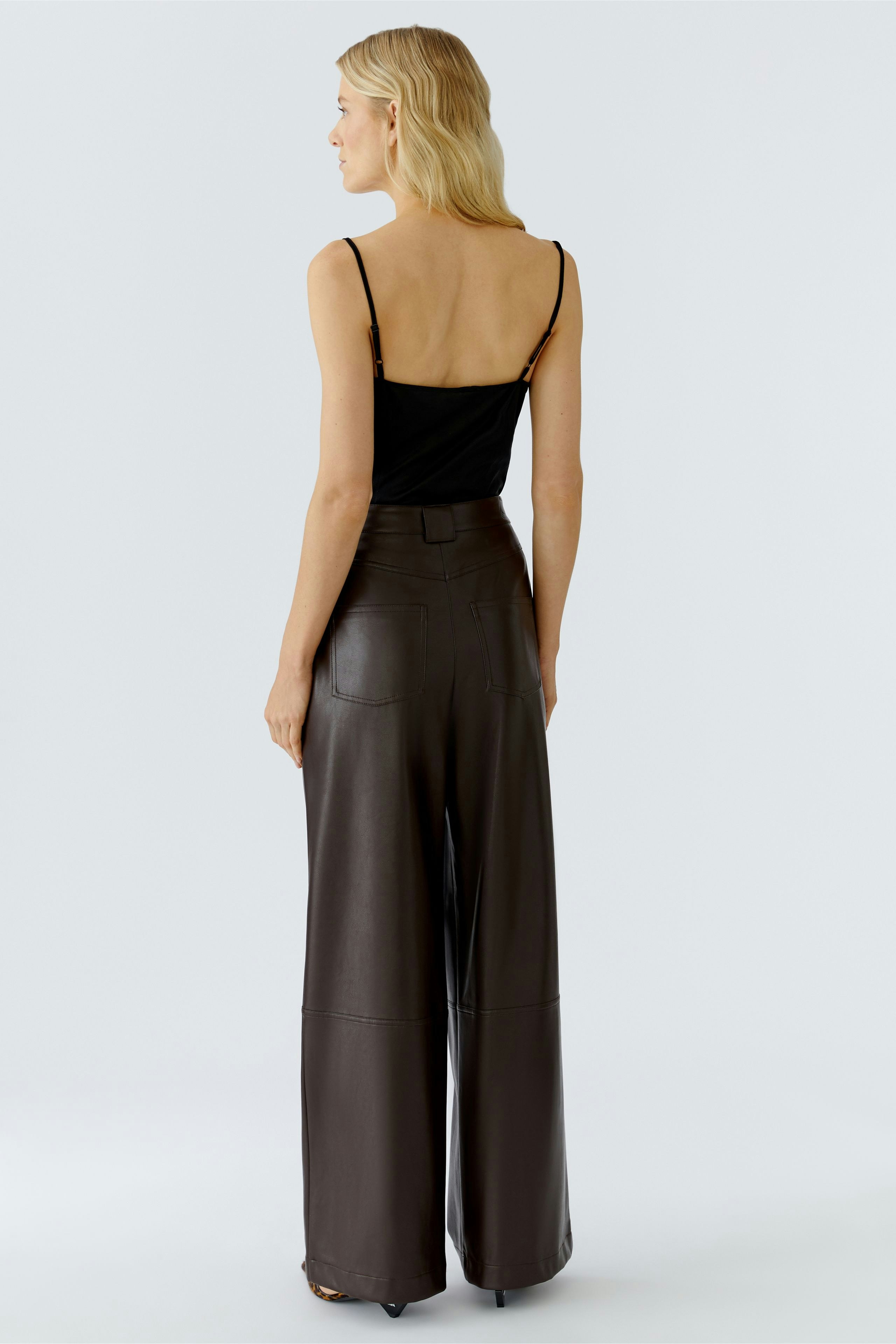 Wide-leg trousers: Woman in brown pleated pants with a relaxed fit, showcasing a casual style.