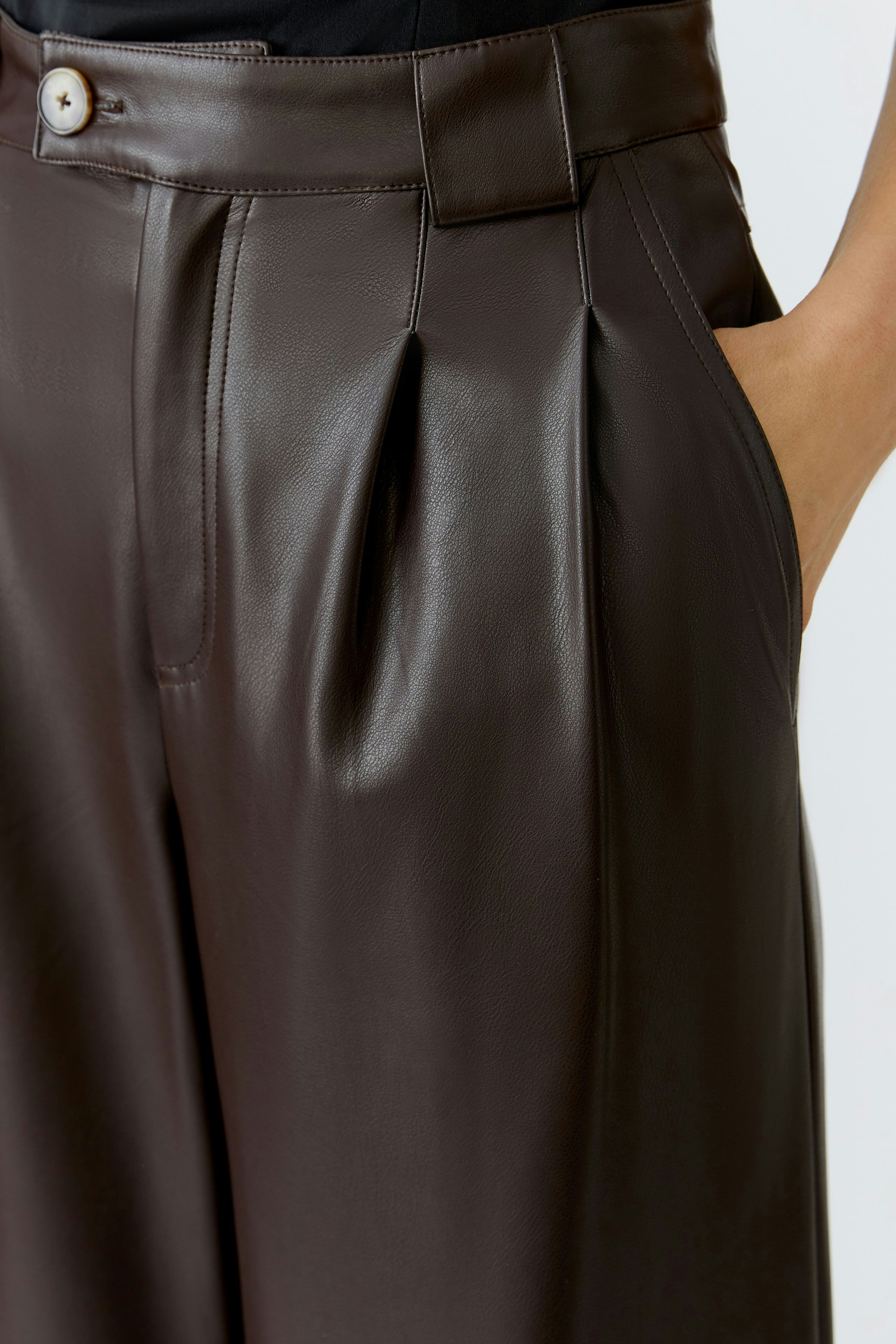 Brown pleated trousers: A woman showcases stylish trousers with a high waist and side pockets.