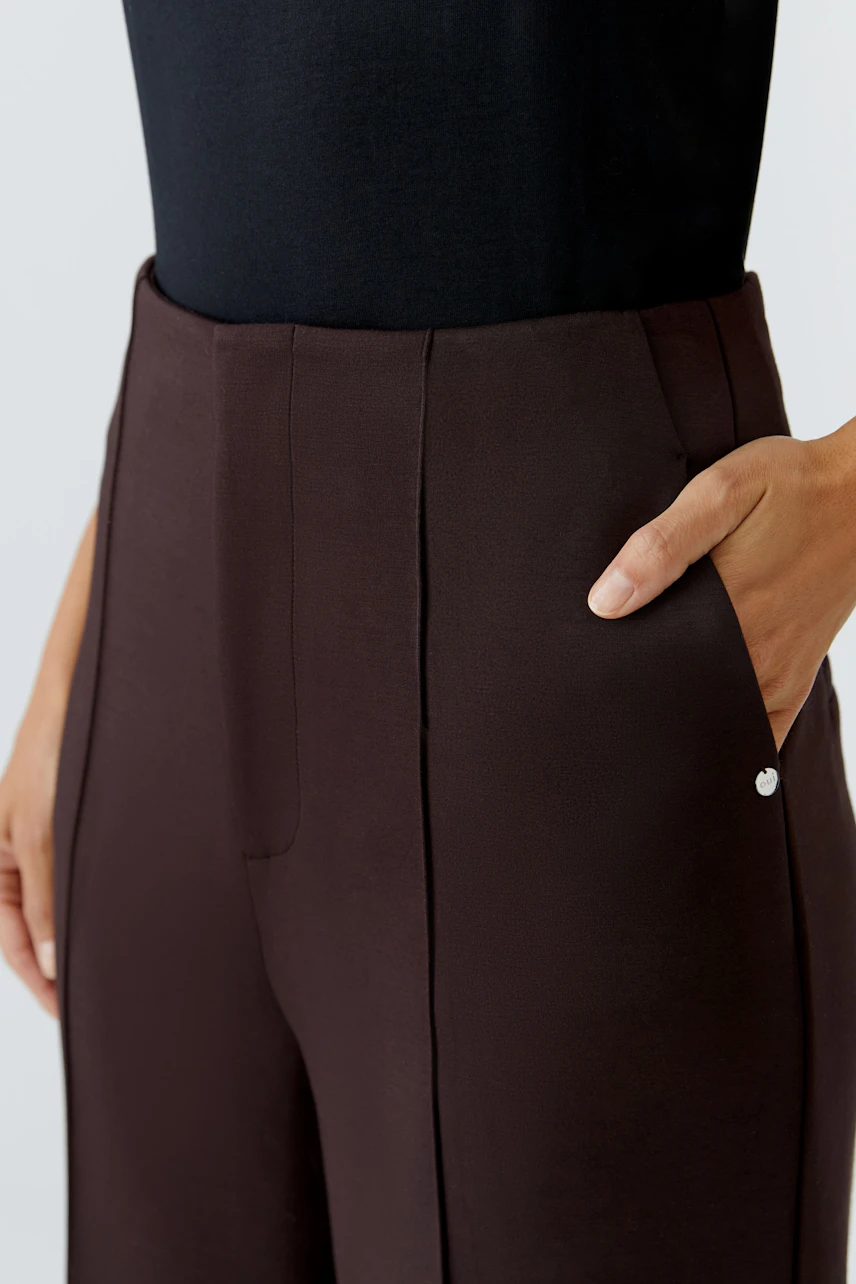 Chic women's trousers: Close-up of a woman wearing dark brown trousers with pockets.