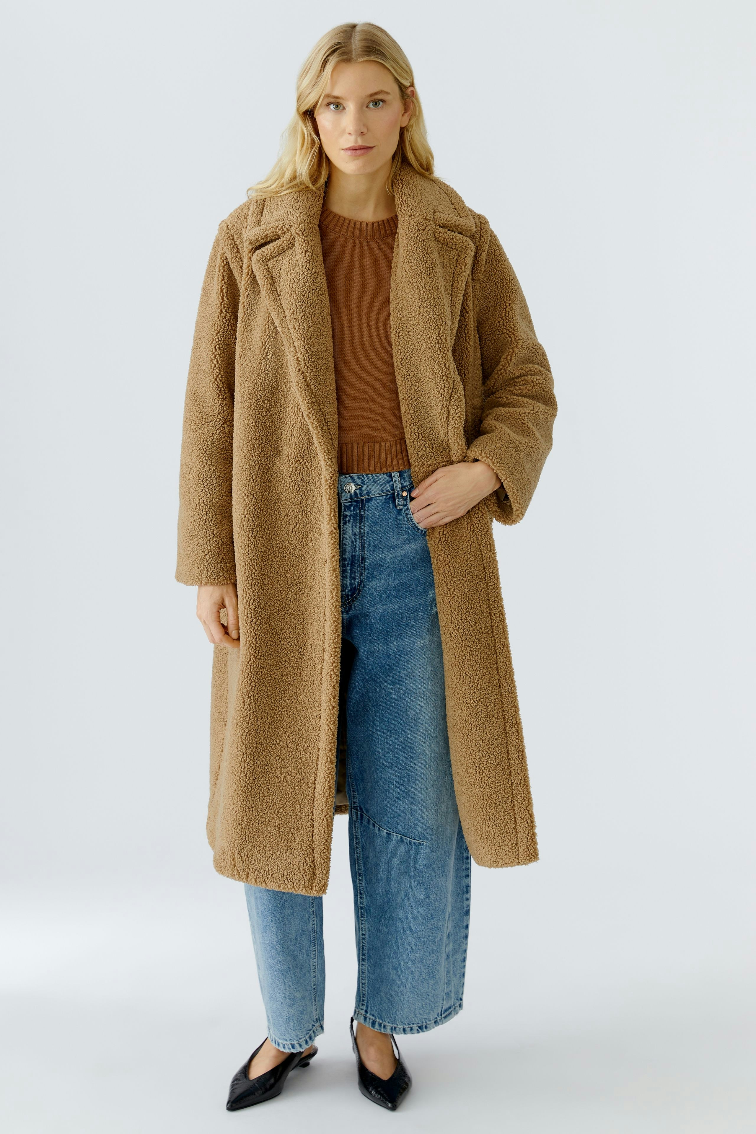 Cozy winter coat: Woman in a soft, brown teddy coat over a brown pullover and blue jeans.