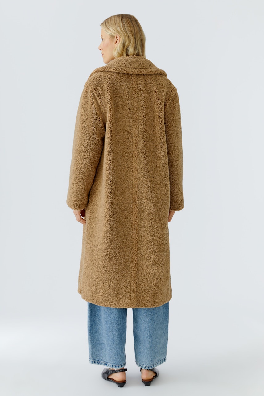 Beiger Wintermantel: Frau mit langem, kuscheligem Mantel und lässigen Jeans steht von hinten.