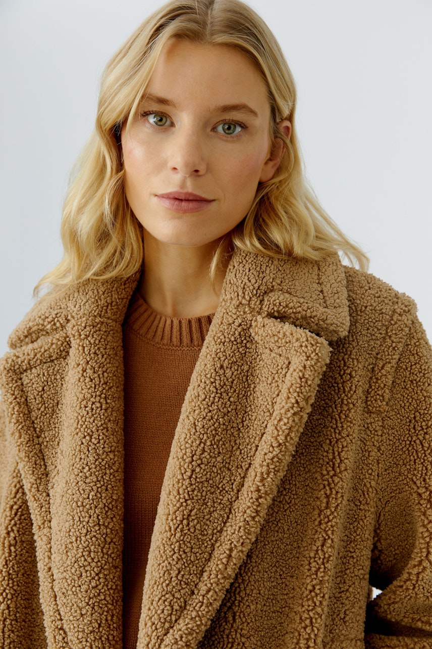 Beiger Wintermantel: Frau mit blonden Haaren trägt einen kuscheligen, weichen Mantel im Teddy-Look.