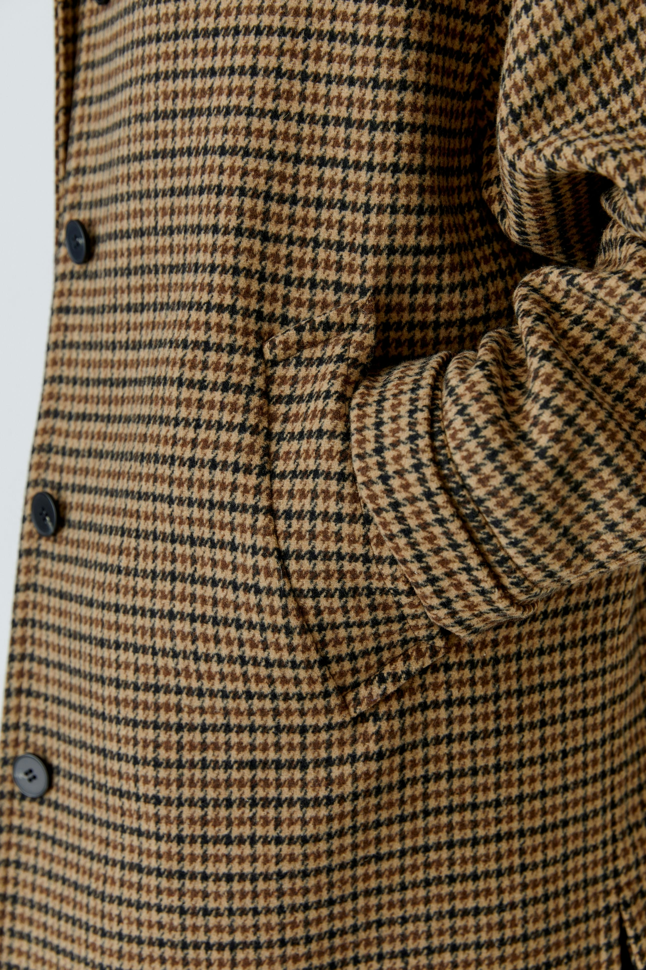 Wool coat: Close-up of a woman's hand in a stylish brown checkered wool coat with pockets.