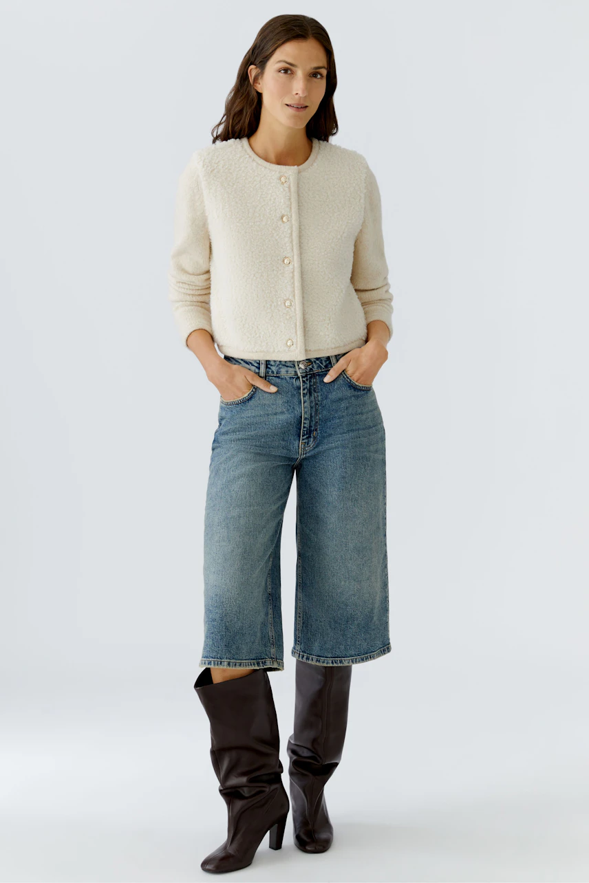 Casual women's cardigan: A woman in a cream cardigan with buttons, paired with jeans and stylish boots.