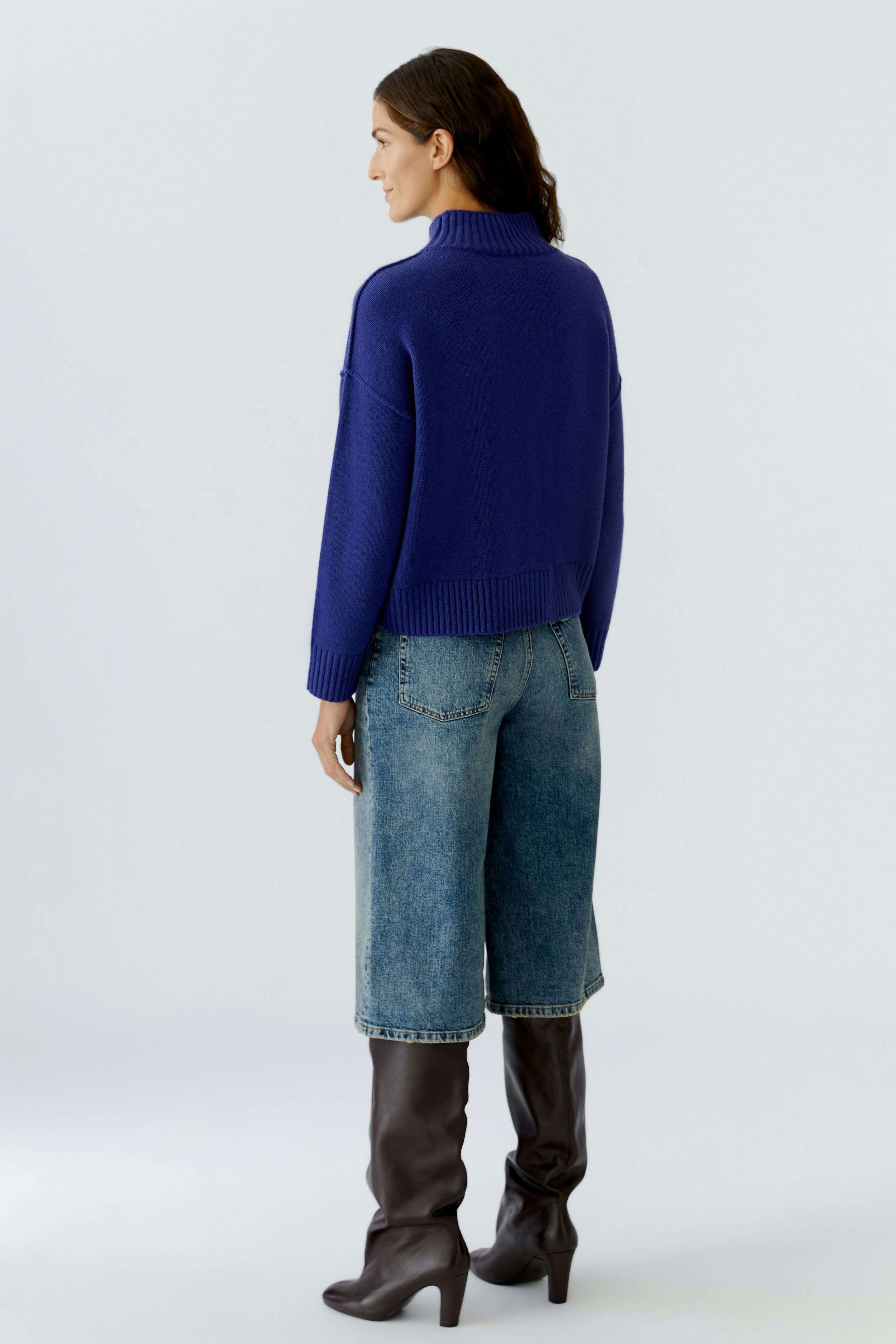 Casual women's pullover: A woman in a blue knit pullover with a high collar, paired with wide jeans.