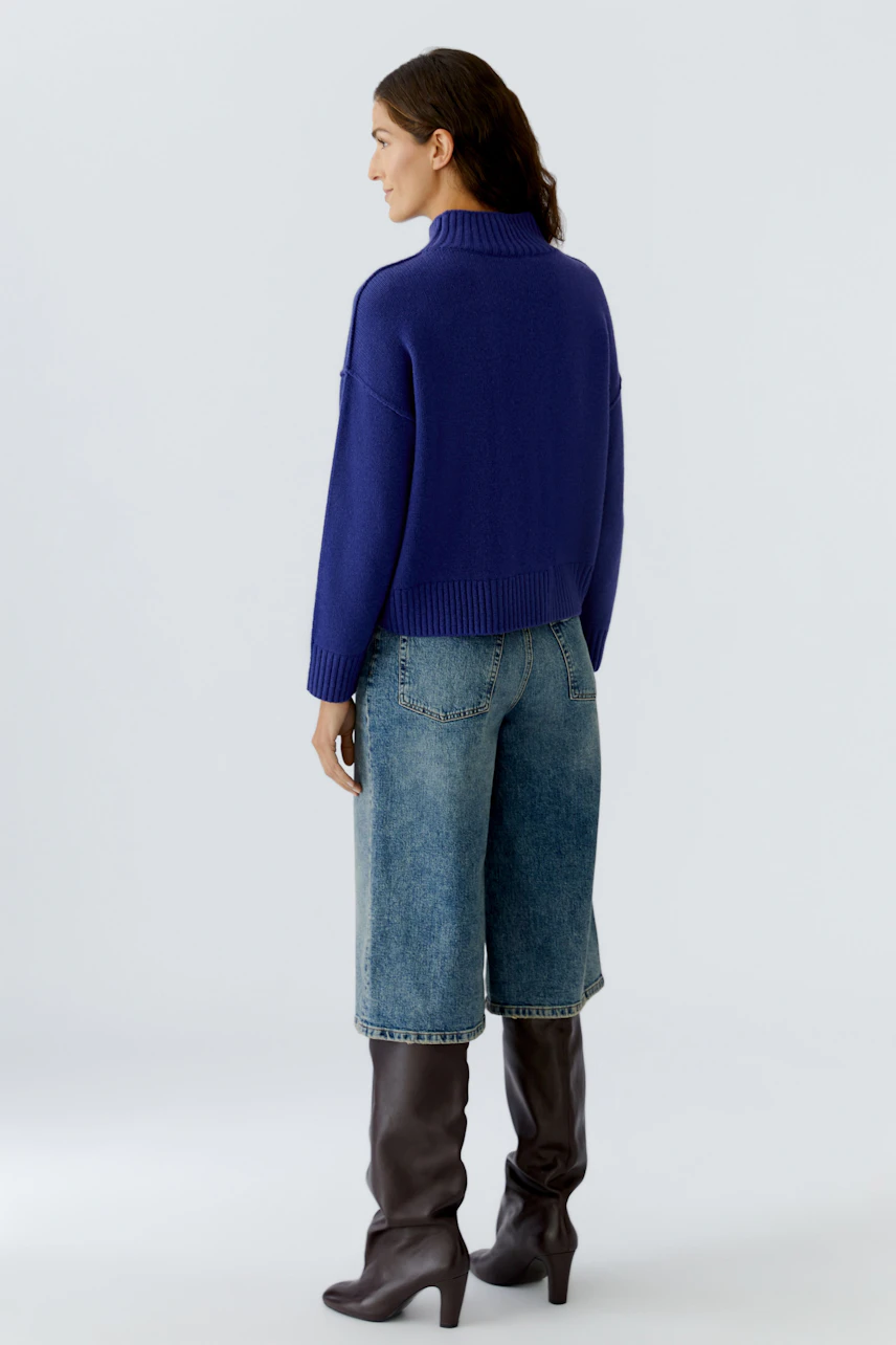 Casual women's pullover: A woman in a blue knit pullover with a high collar, paired with wide jeans.
