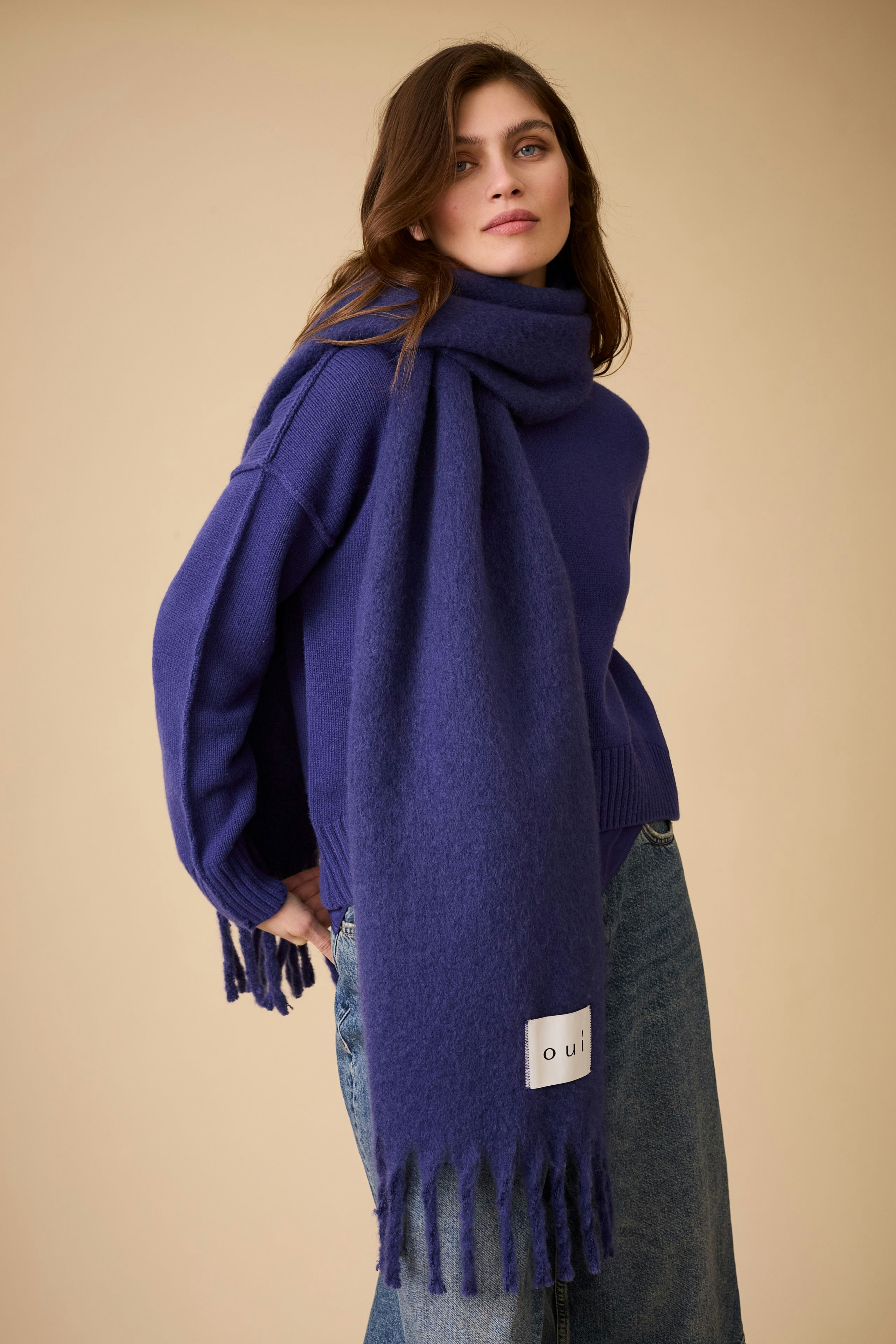 Casual women's pullover: Young woman in a purple pullover with a matching scarf, styled with relaxed jeans.