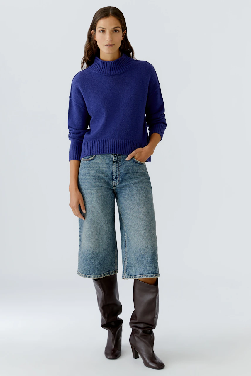 Casual women's pullover: A woman in a blue knit pullover with a high neck and relaxed fit, paired with wide jeans.