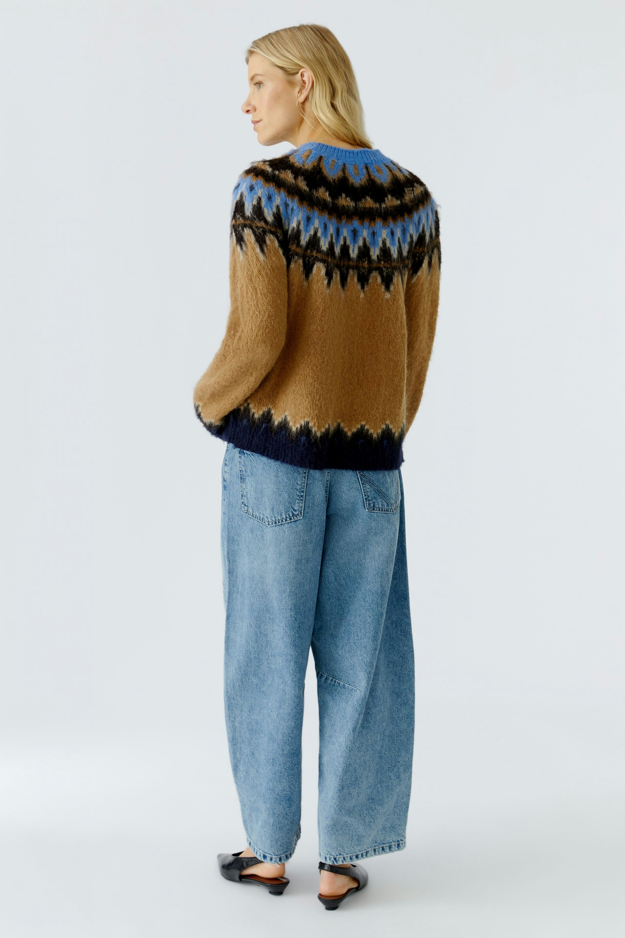Cozy women's pullover: A woman in a colorful knit pullover with a relaxed fit and wide jeans.