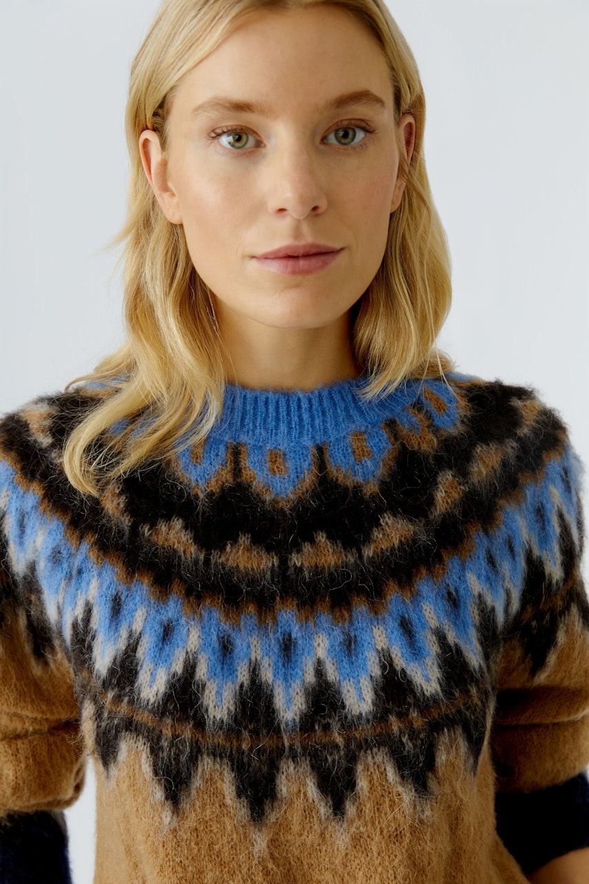 Damen-Pullover: Frau trägt einen braun-blauen Strickpullover mit auffälligem Muster und lässigem Schnitt.