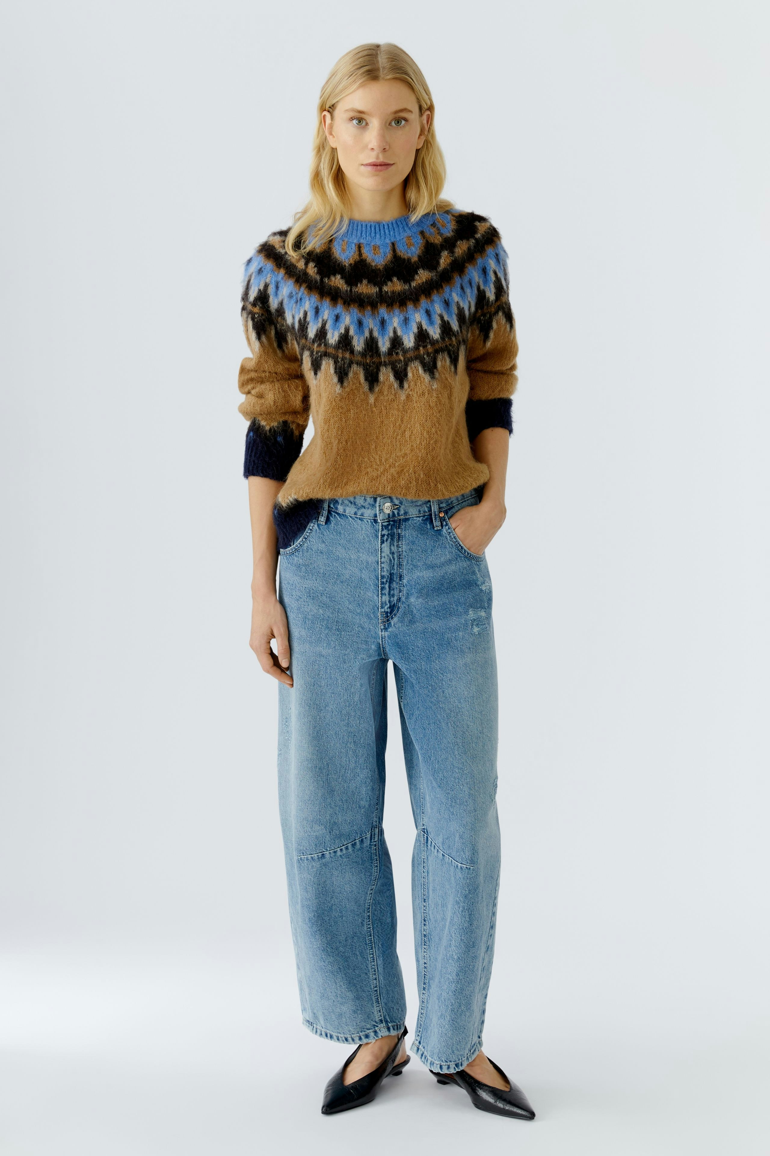 Casual women's pullover: Young woman in a brown patterned pullover with blue accents and relaxed jeans.