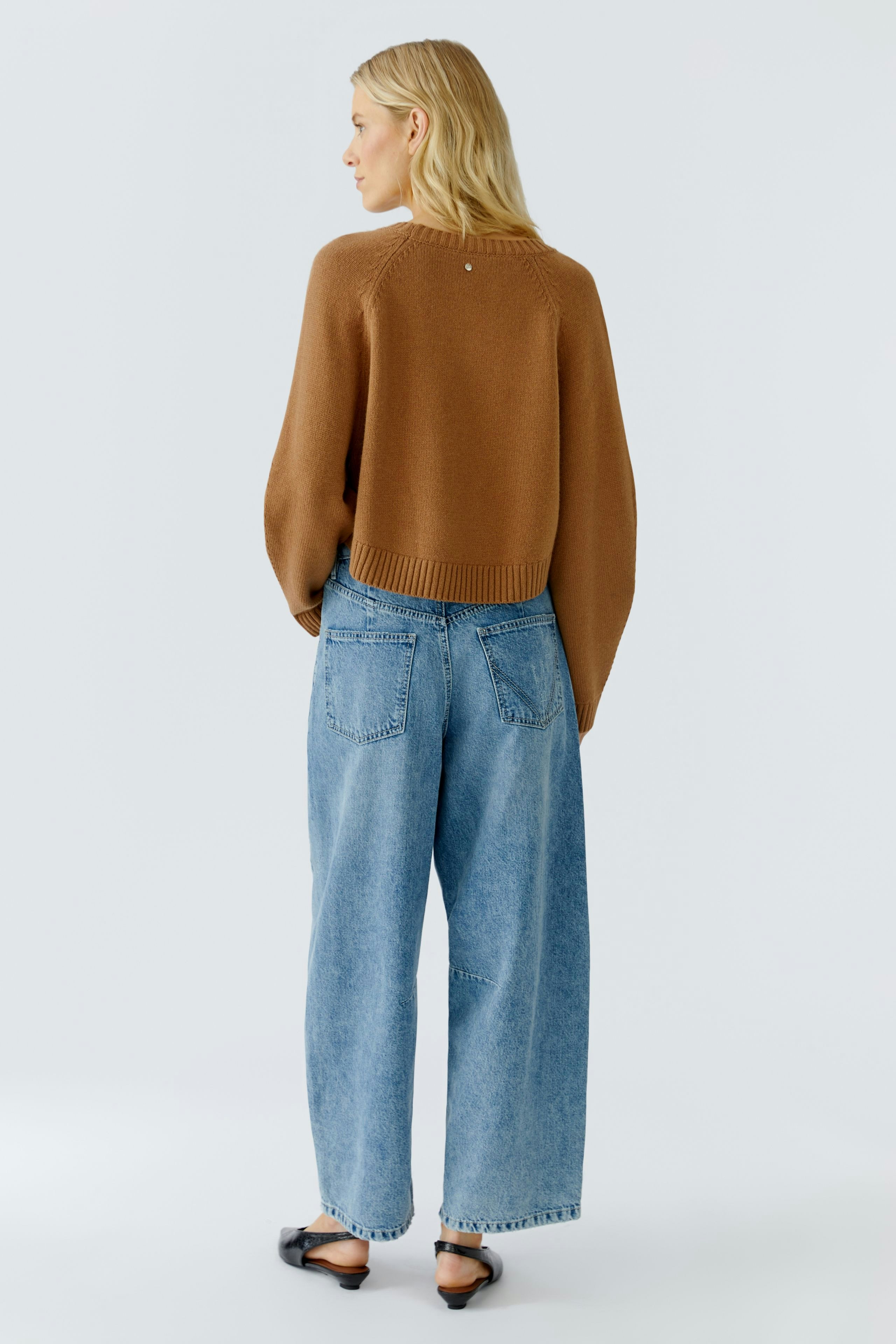 Casual women's pullover: A woman in a brown knitted pullover and loose jeans, showcasing a relaxed style.
