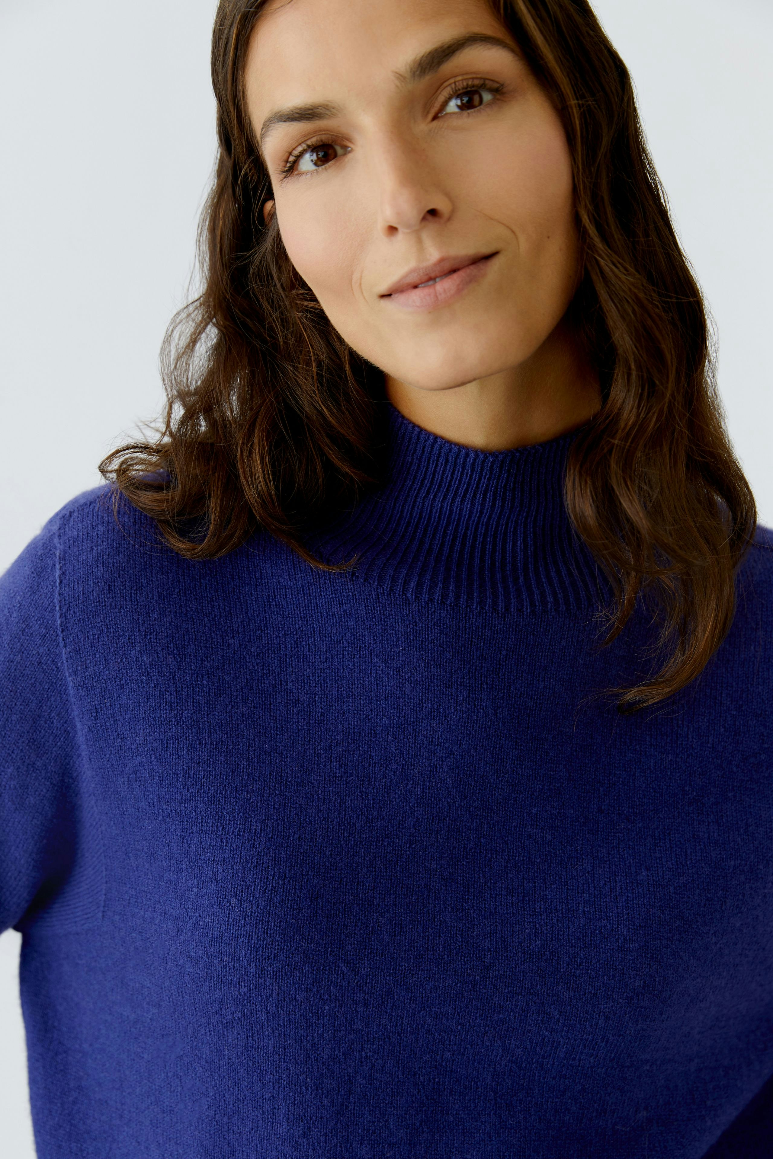 Casual women's pullover: Woman in a cozy blue pullover with a high neck, smiling softly.