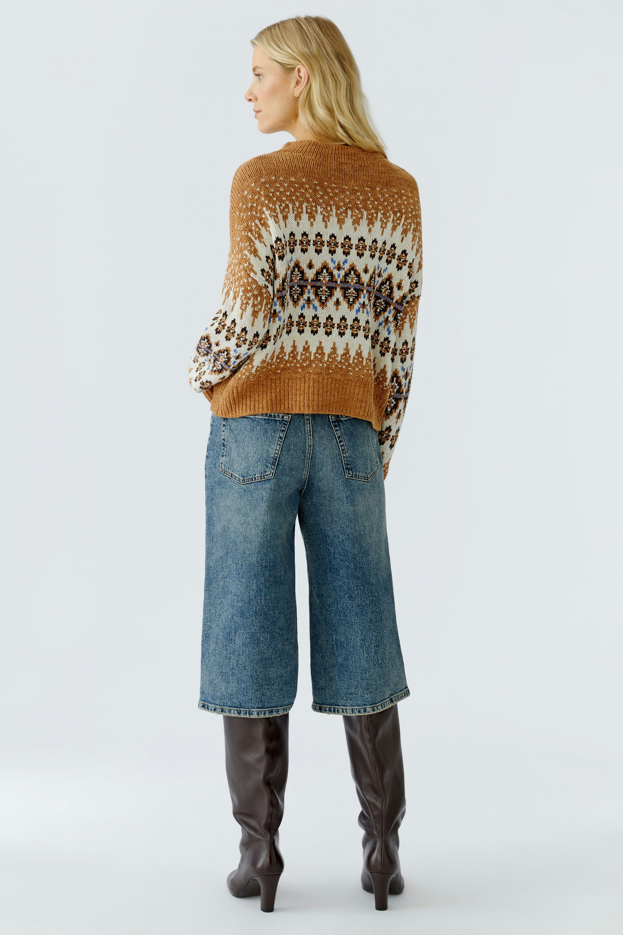 Casual women's pullover: A woman in a cozy, patterned brown pullover with relaxed fit and wide jeans.