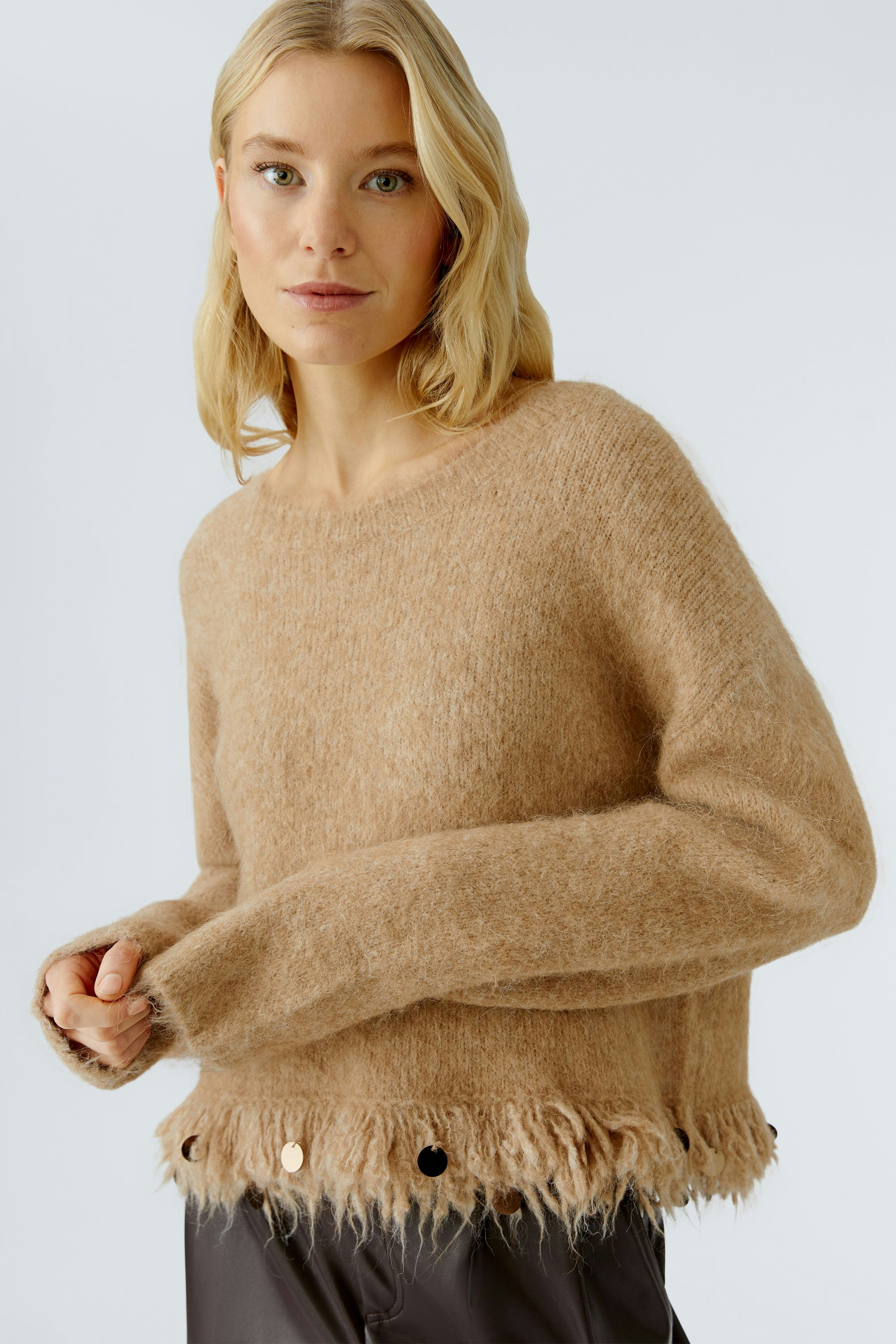 Casual women's pullover: A woman in a soft beige pullover with a fringed hem and decorative buttons.