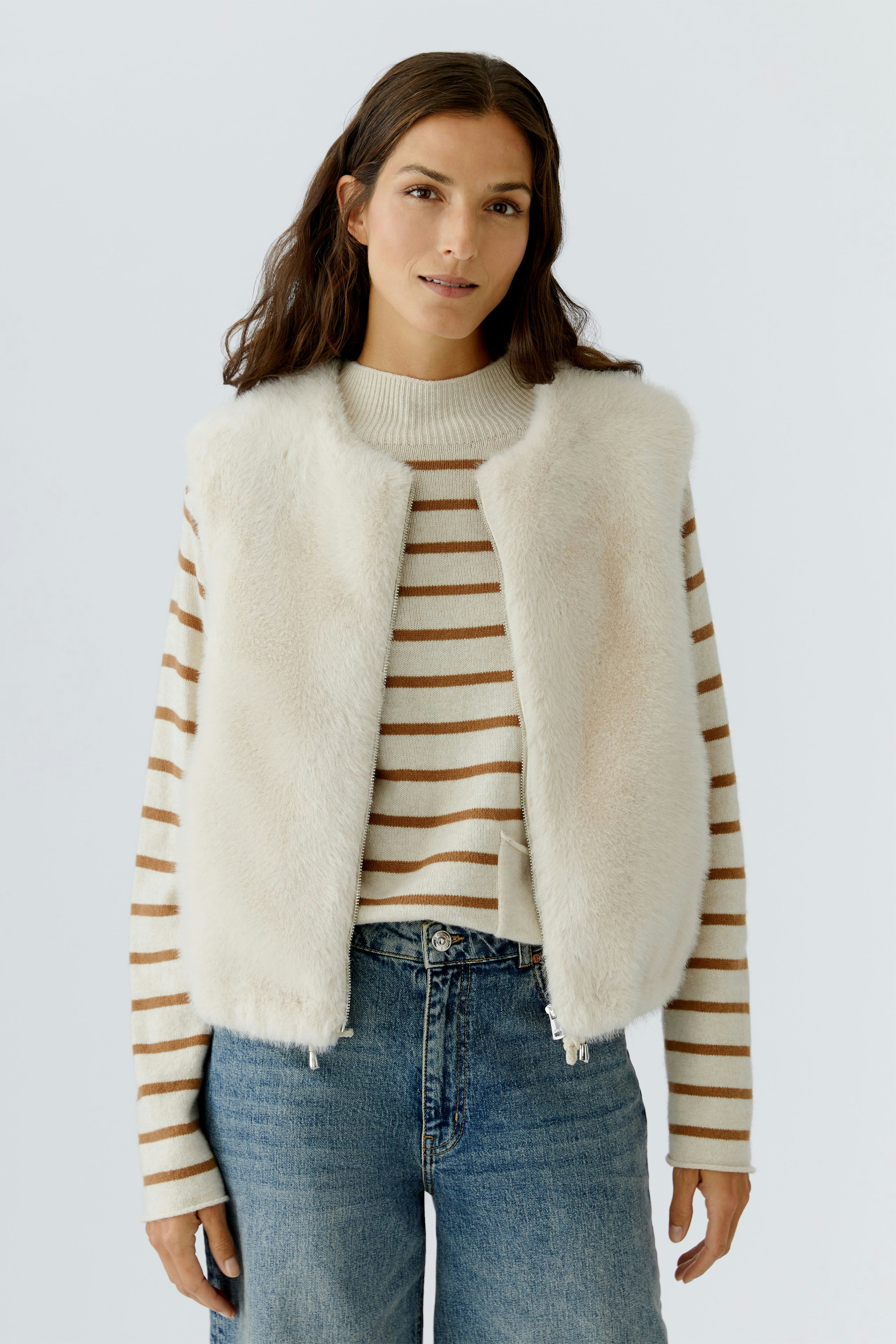 Casual women's vest: A woman in a soft, cream vest over a striped pullover and jeans.