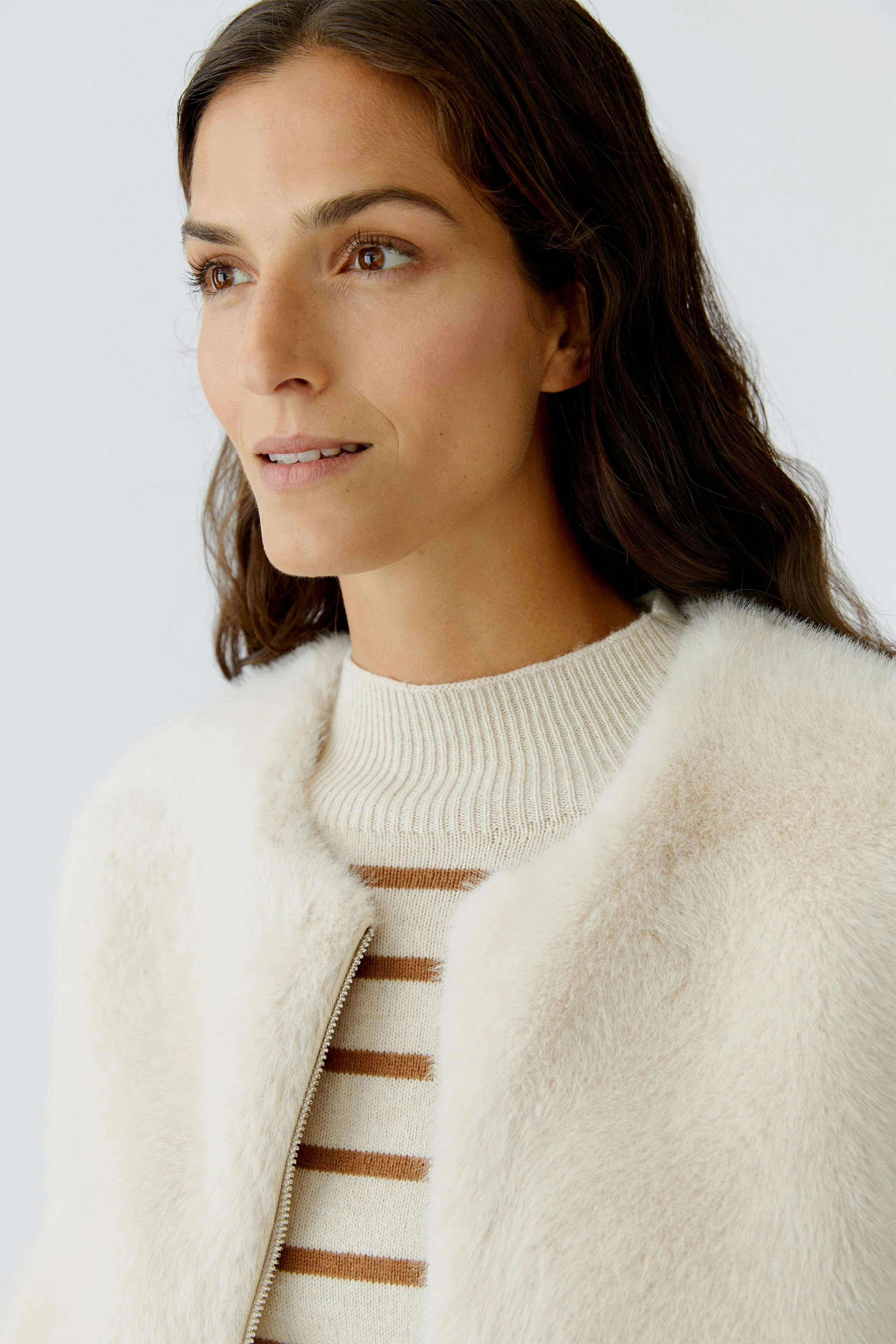 Modern women's vest: Woman in a soft, cream-colored vest over a striped pullover, looking confidently.
