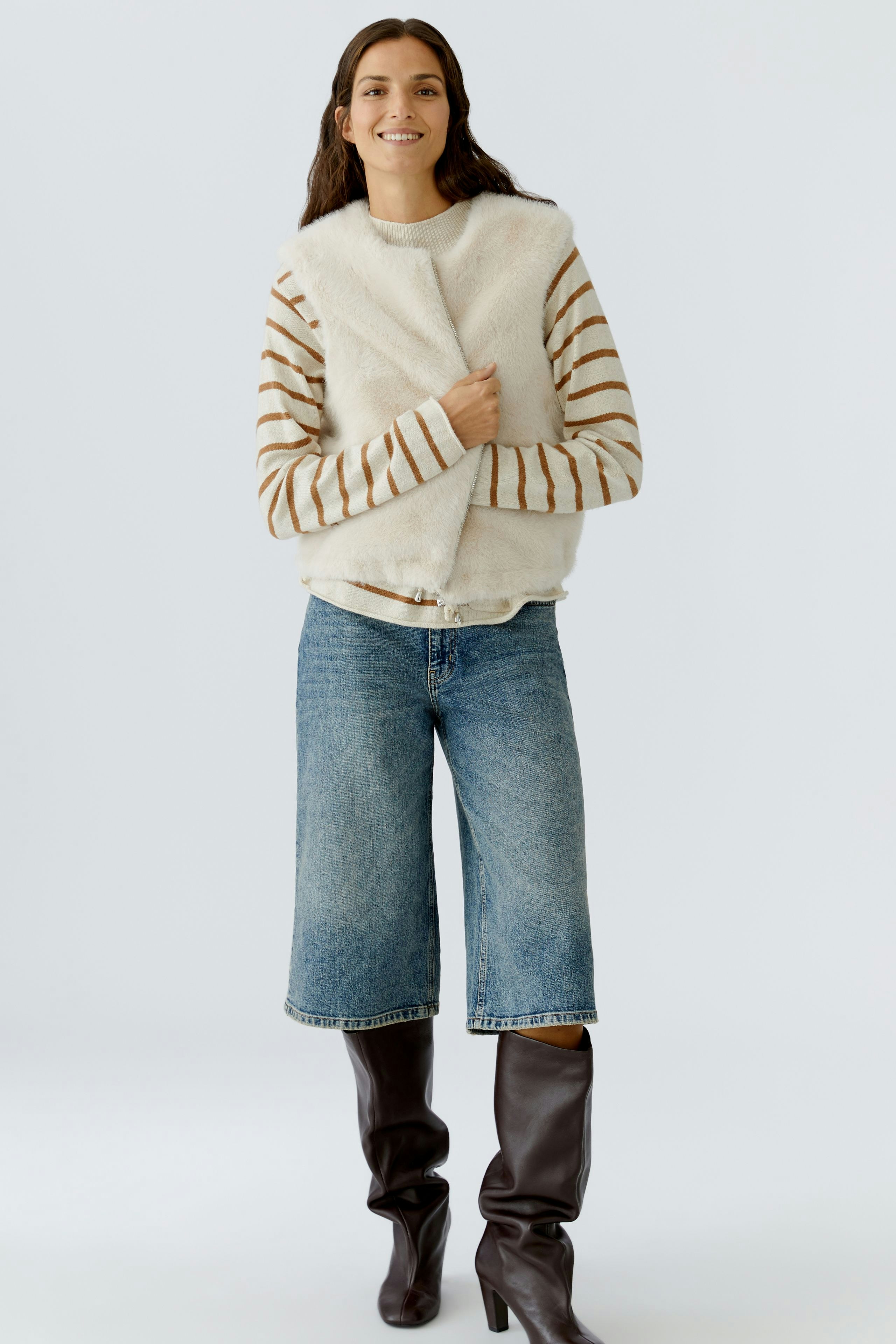 Casual women's vest: Smiling woman in a fluffy white vest over a striped pullover and wide jeans.