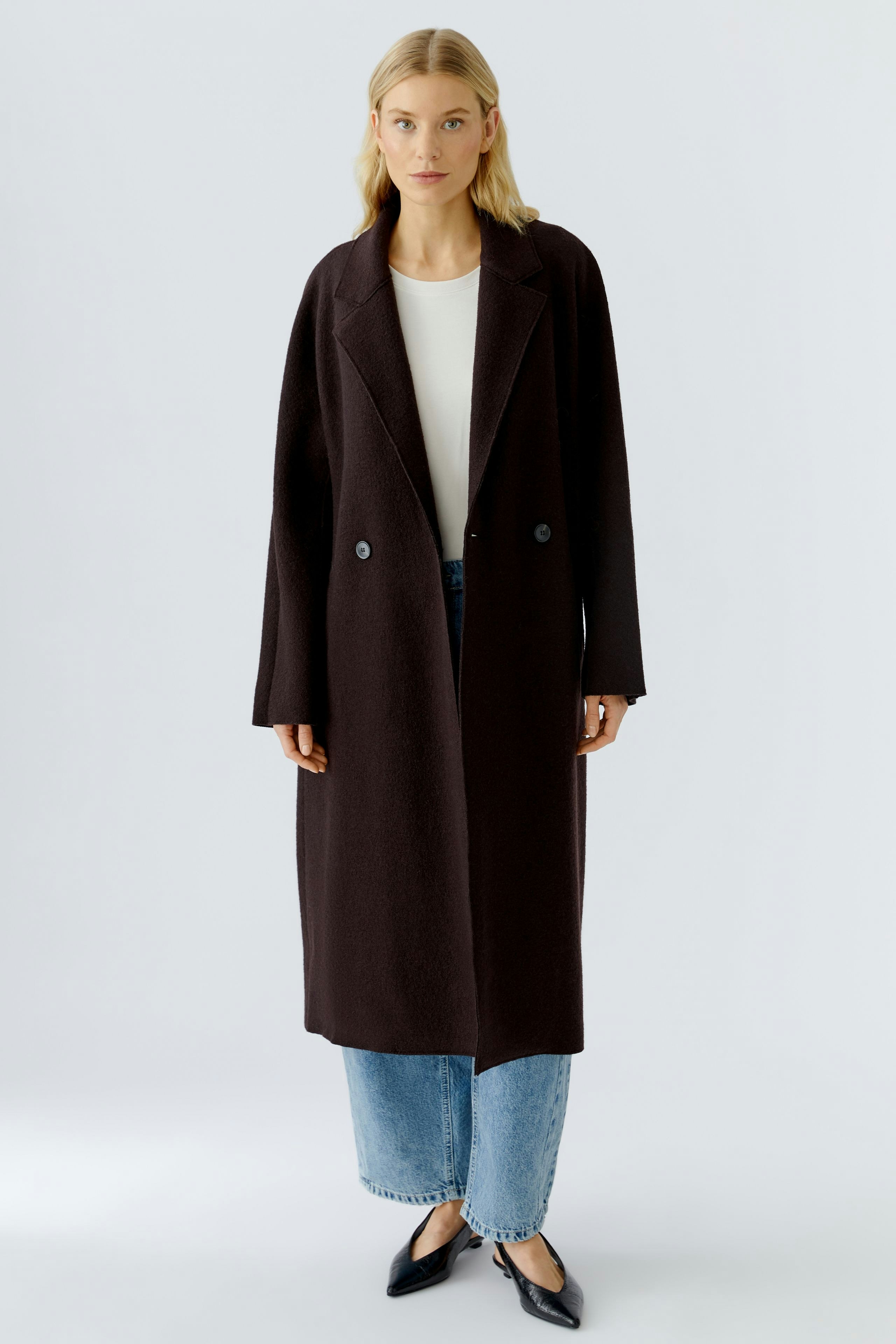 Stylish women's winter coat: A woman in a long, dark coat over a white top and jeans.