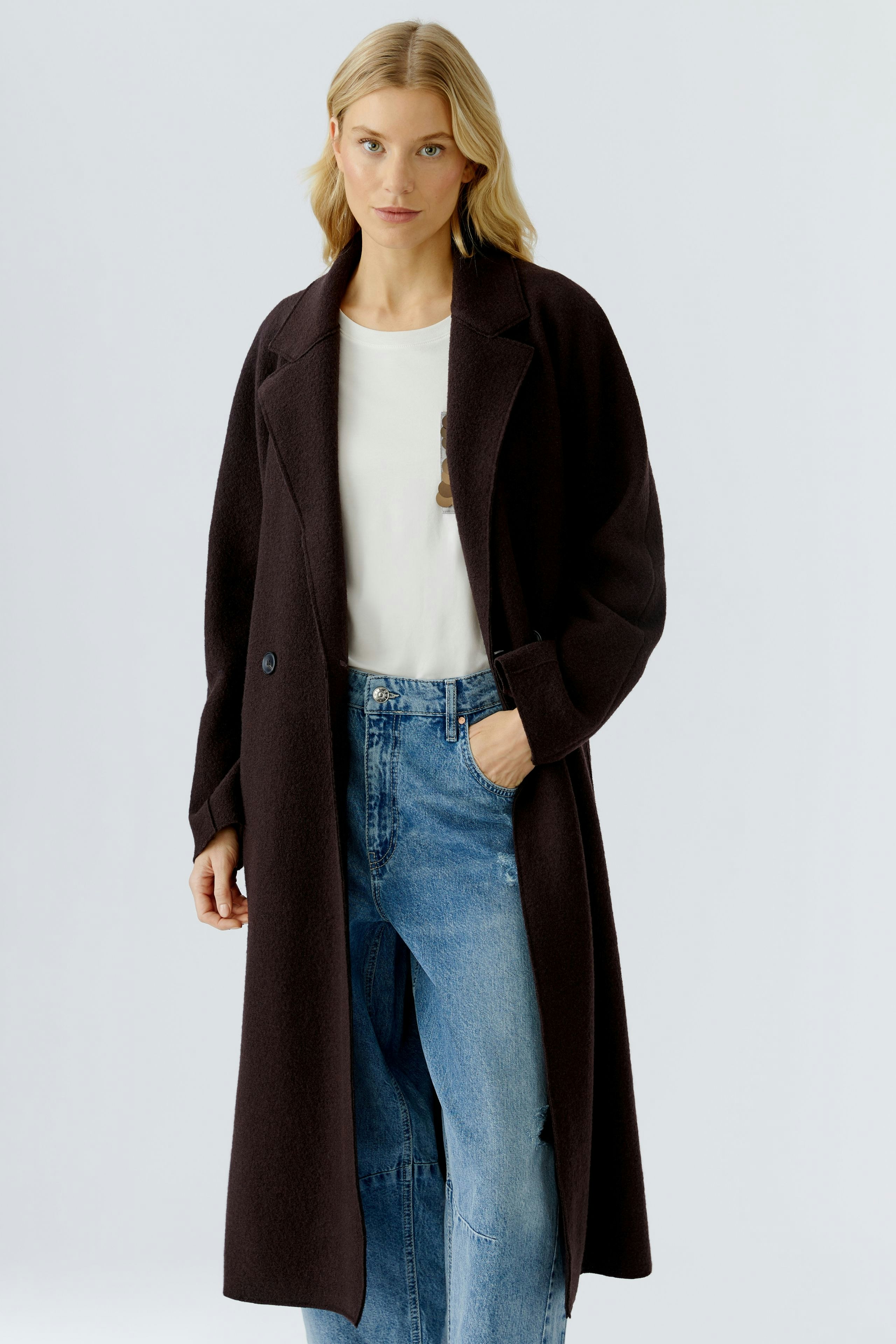 Stylish women's winter coat: A woman in a long, dark coat over a white top and blue jeans.