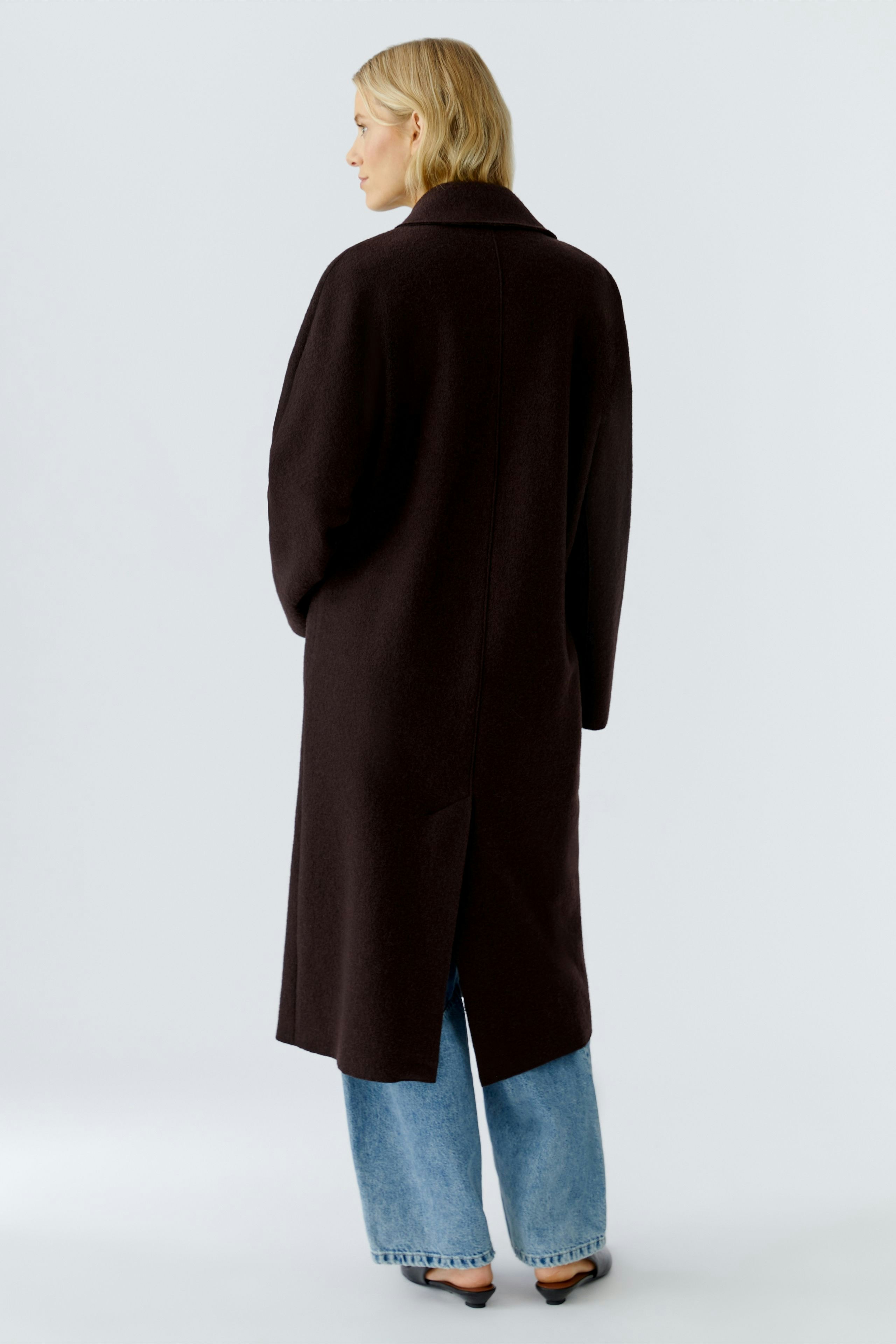 Stylish women's winter coat: A woman in a long, dark coat with a relaxed fit and back slit.