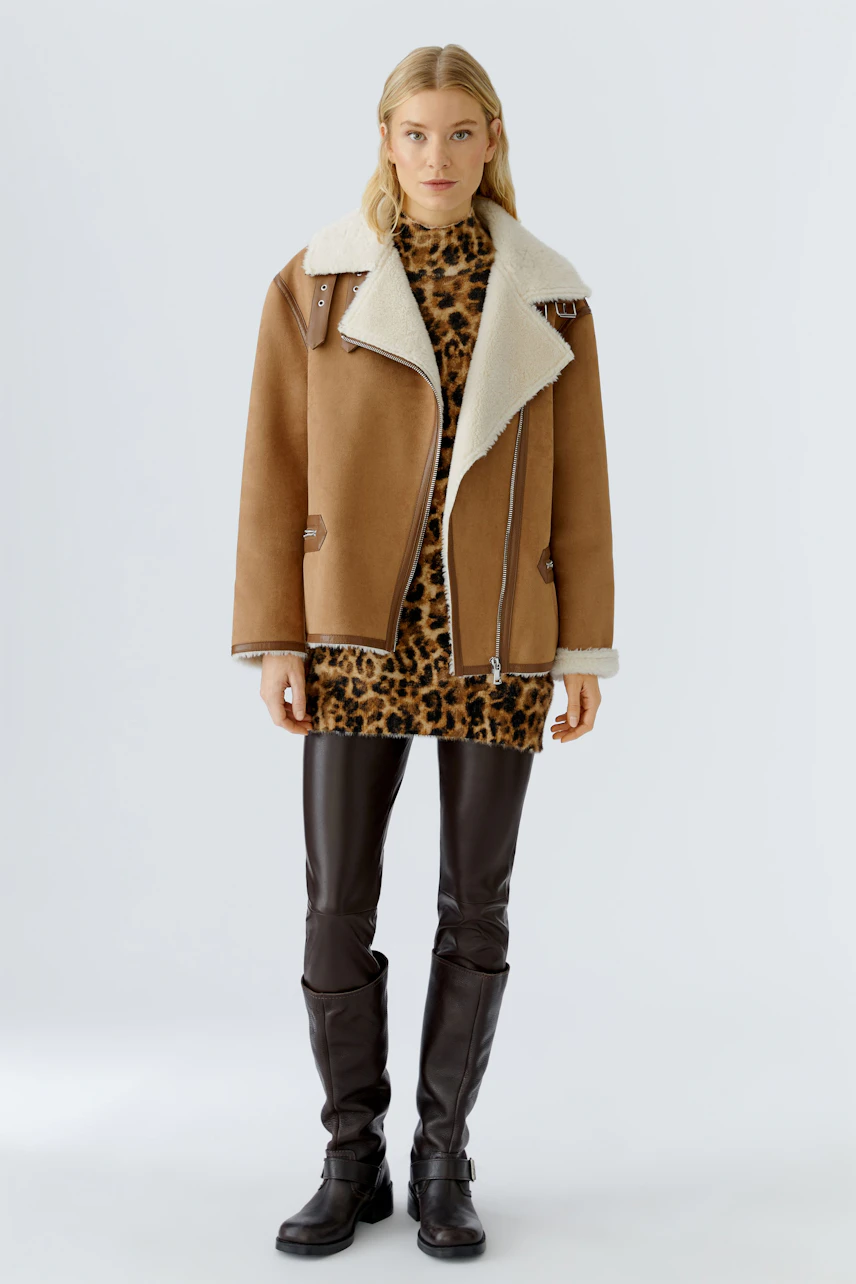 Casual outdoor jacket: Woman in a brown shearling jacket over a leopard print dress, exuding a relaxed vibe.