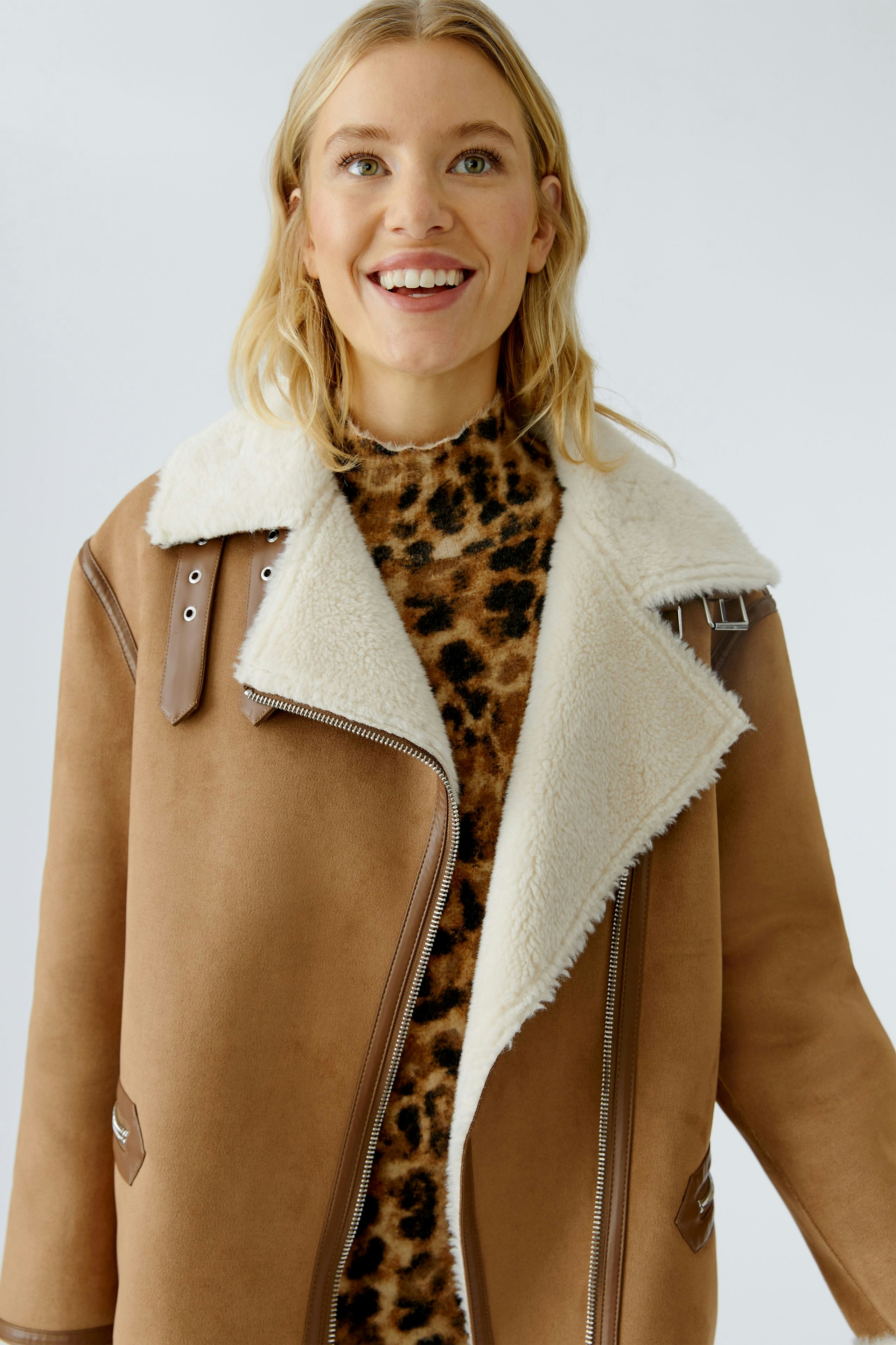 Casual outdoor jacket: Woman in a brown jacket with a fluffy collar, smiling and wearing a leopard print top.
