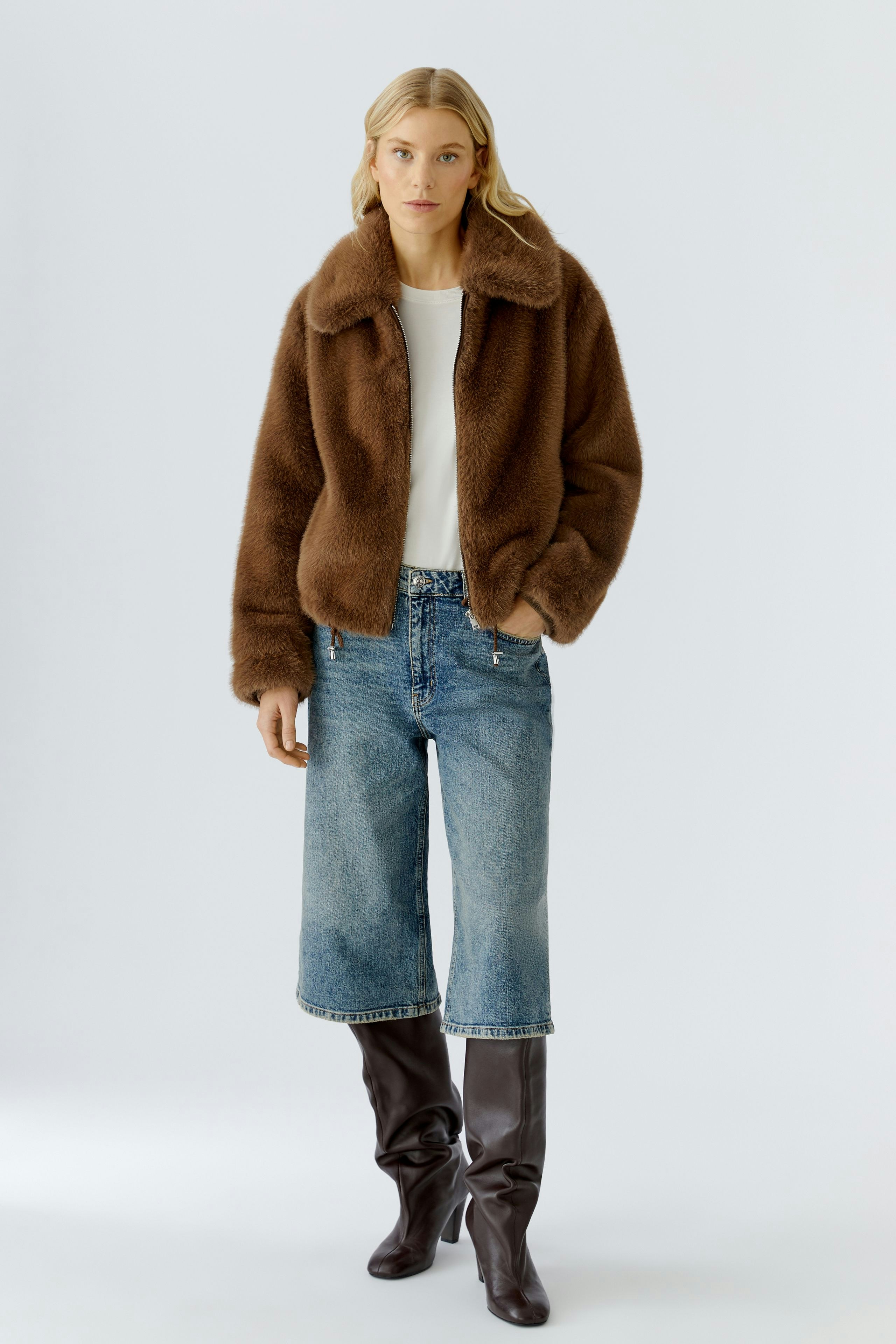 Cozy women's jacket: A woman in a brown fluffy jacket paired with jeans and knee-high boots.