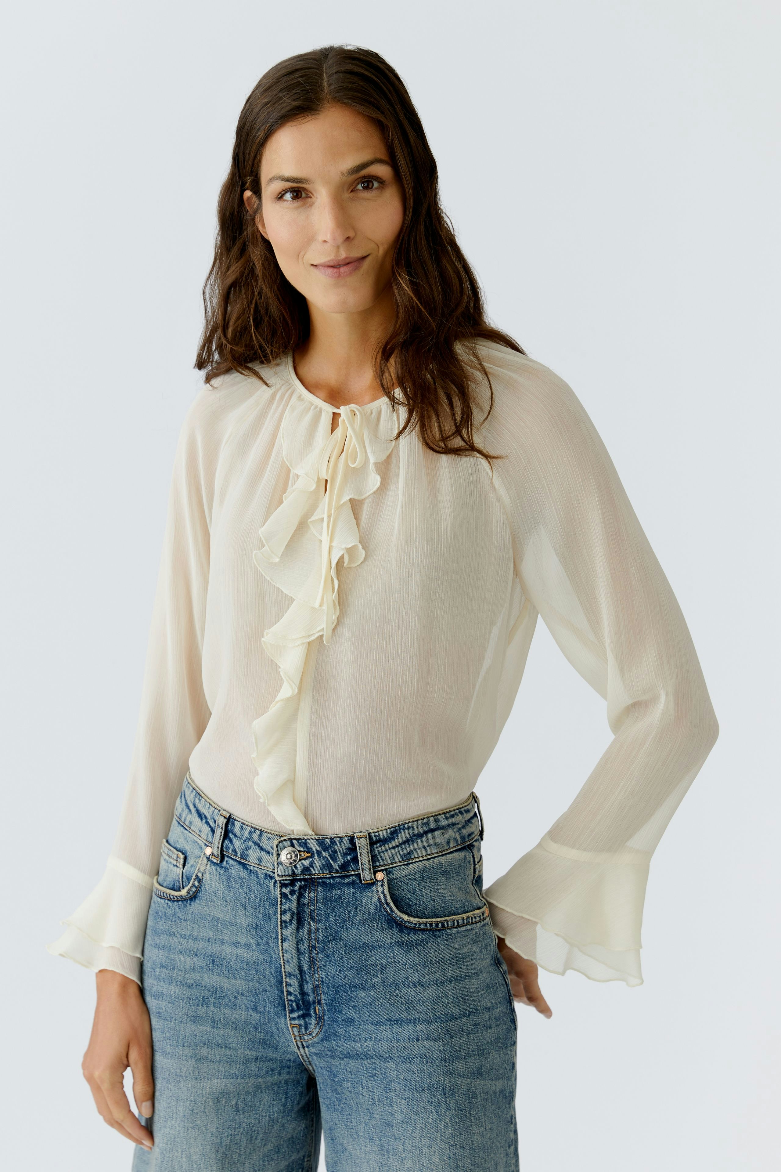 Light blouse with ruffles: Woman in a cream blouse with flared sleeves and casual jeans.