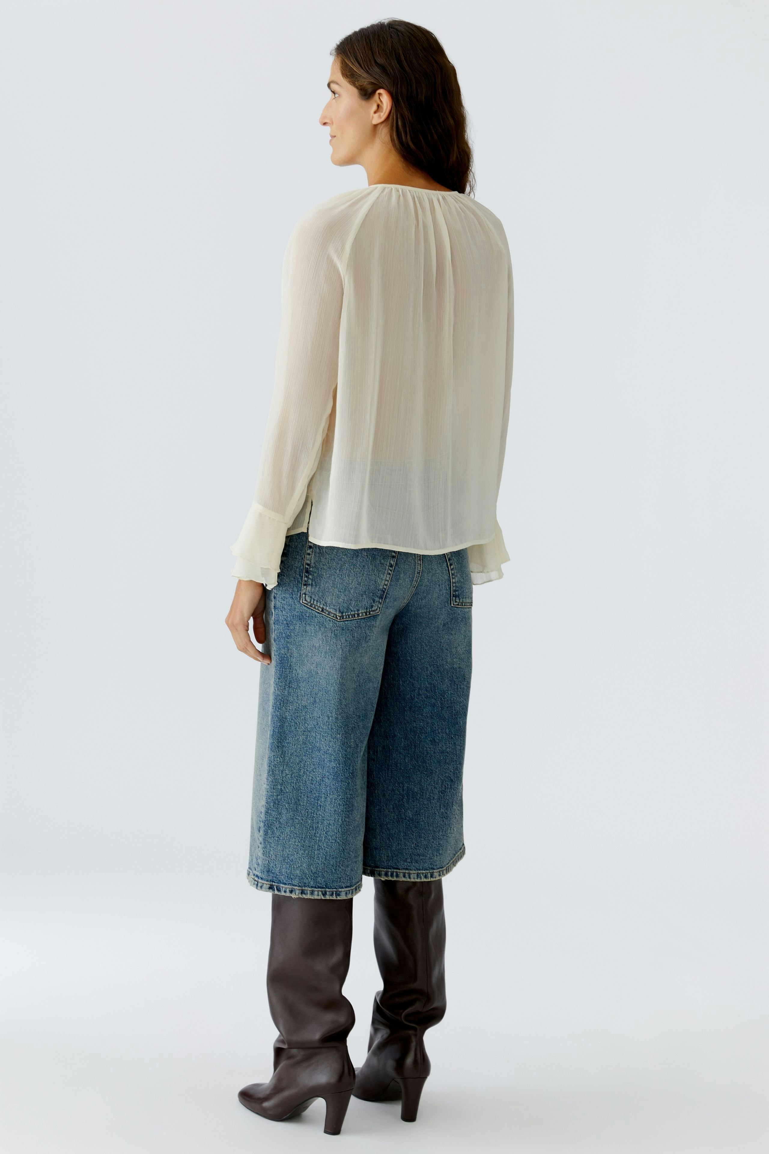 Light blouse: Woman in a flowing cream blouse paired with denim culottes and knee-high boots.