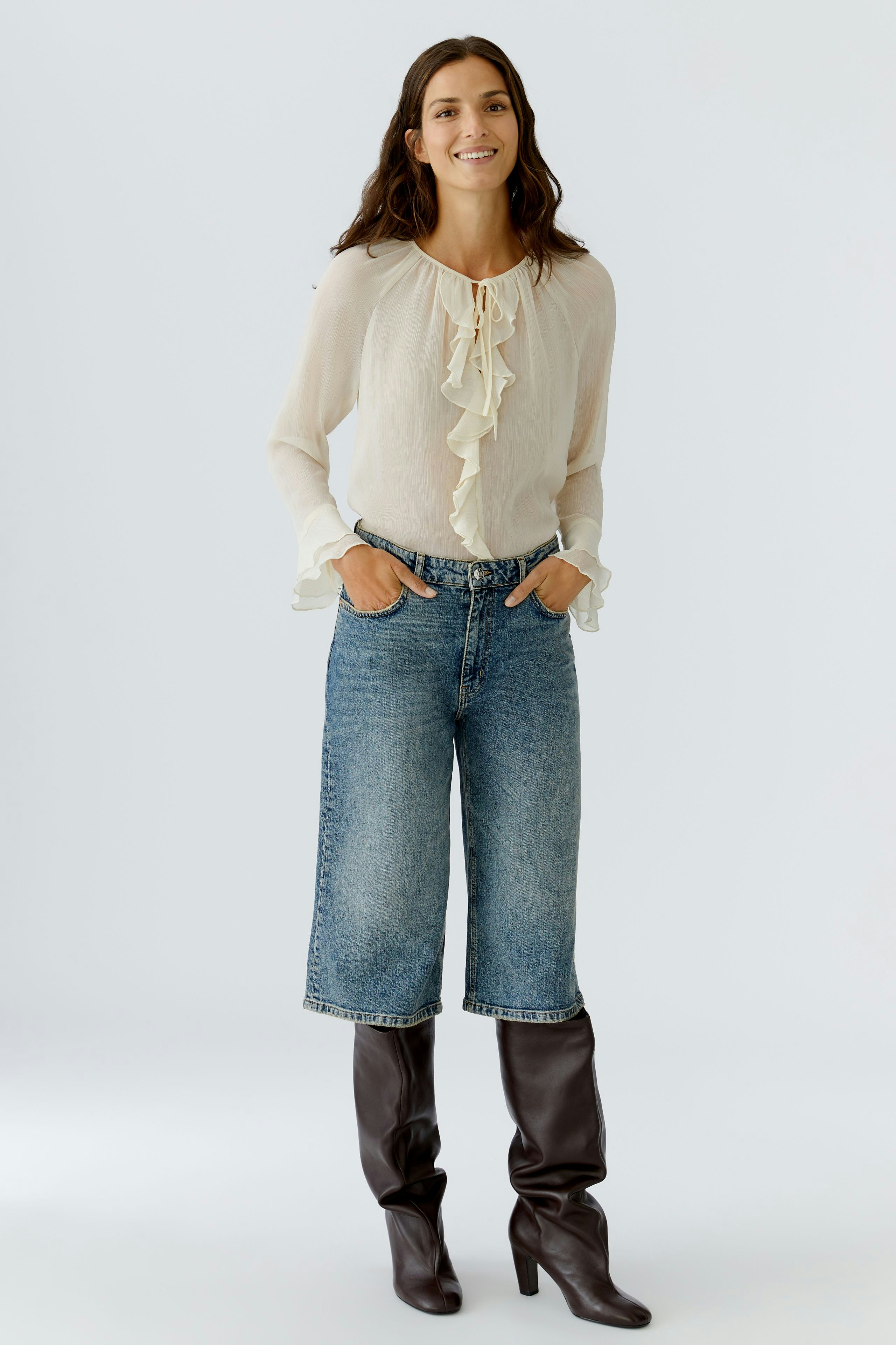 Light blouse with ruffles: Woman in a flowing cream blouse, paired with relaxed denim and knee-high boots.