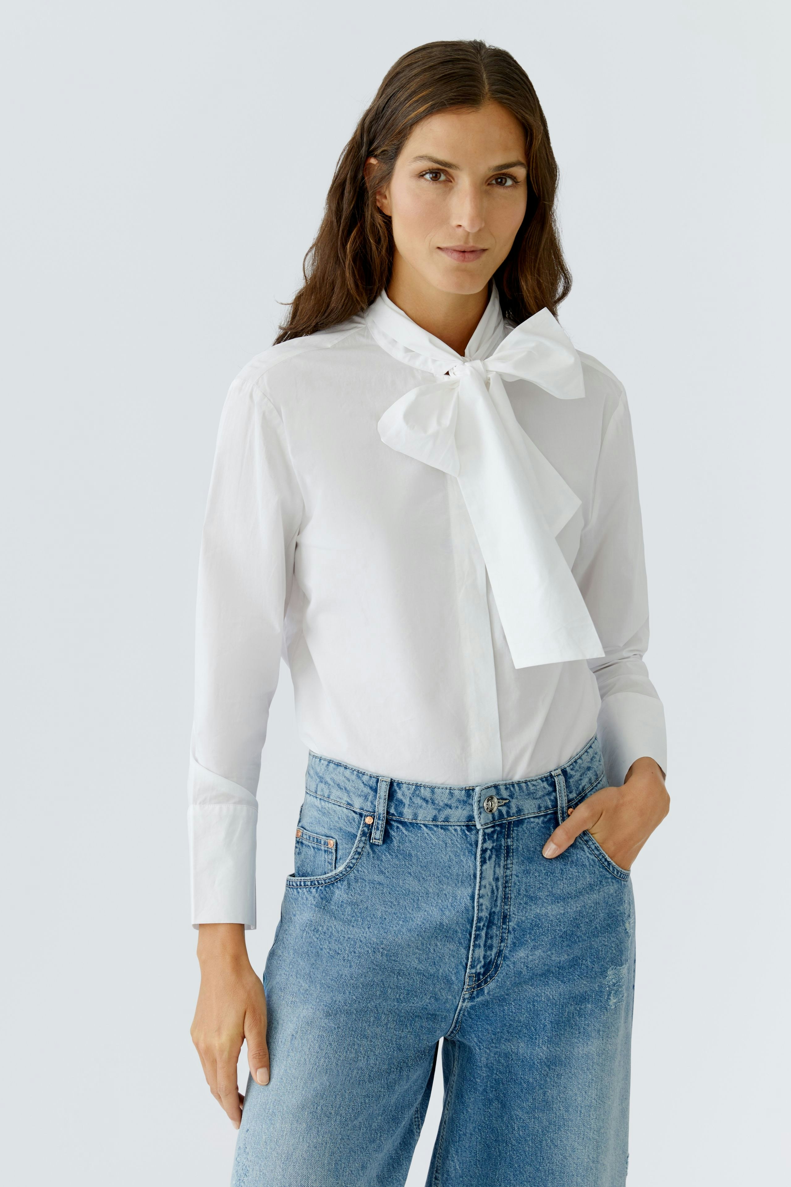 Modern women's blouse: Woman in a white blouse with a bow tie, paired with casual blue jeans.