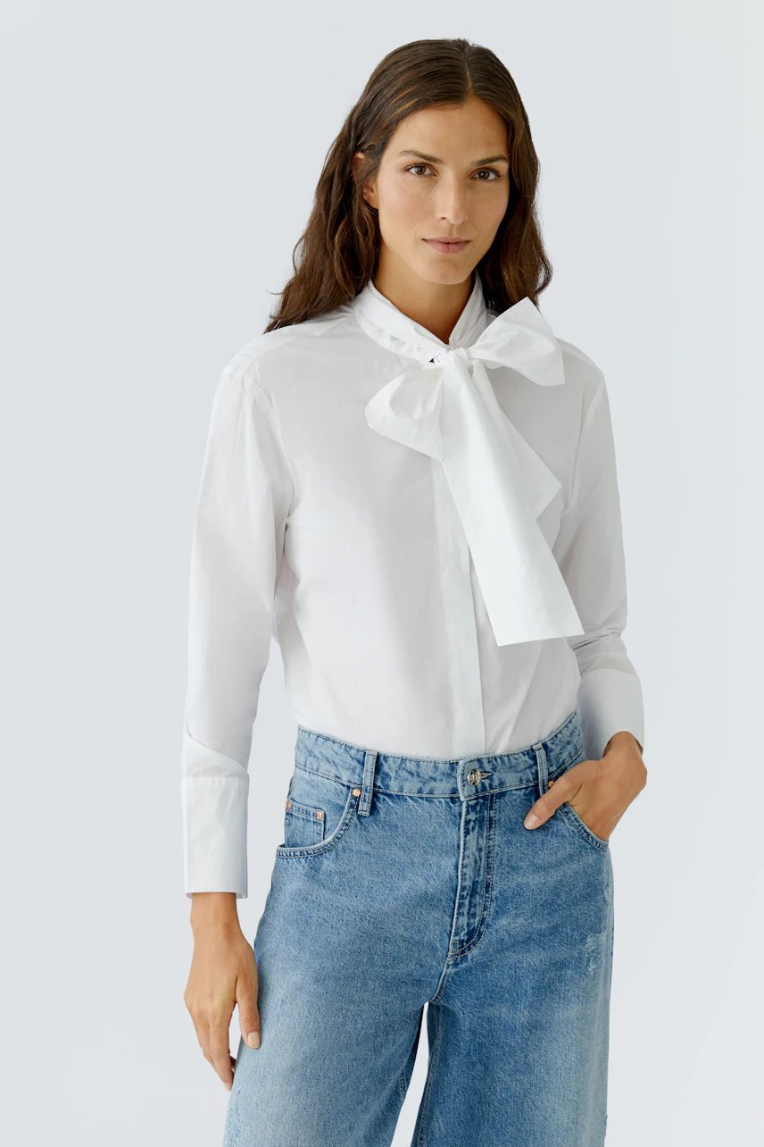 Modern women's blouse: Woman in a white blouse with a bow tie, paired with casual blue jeans.