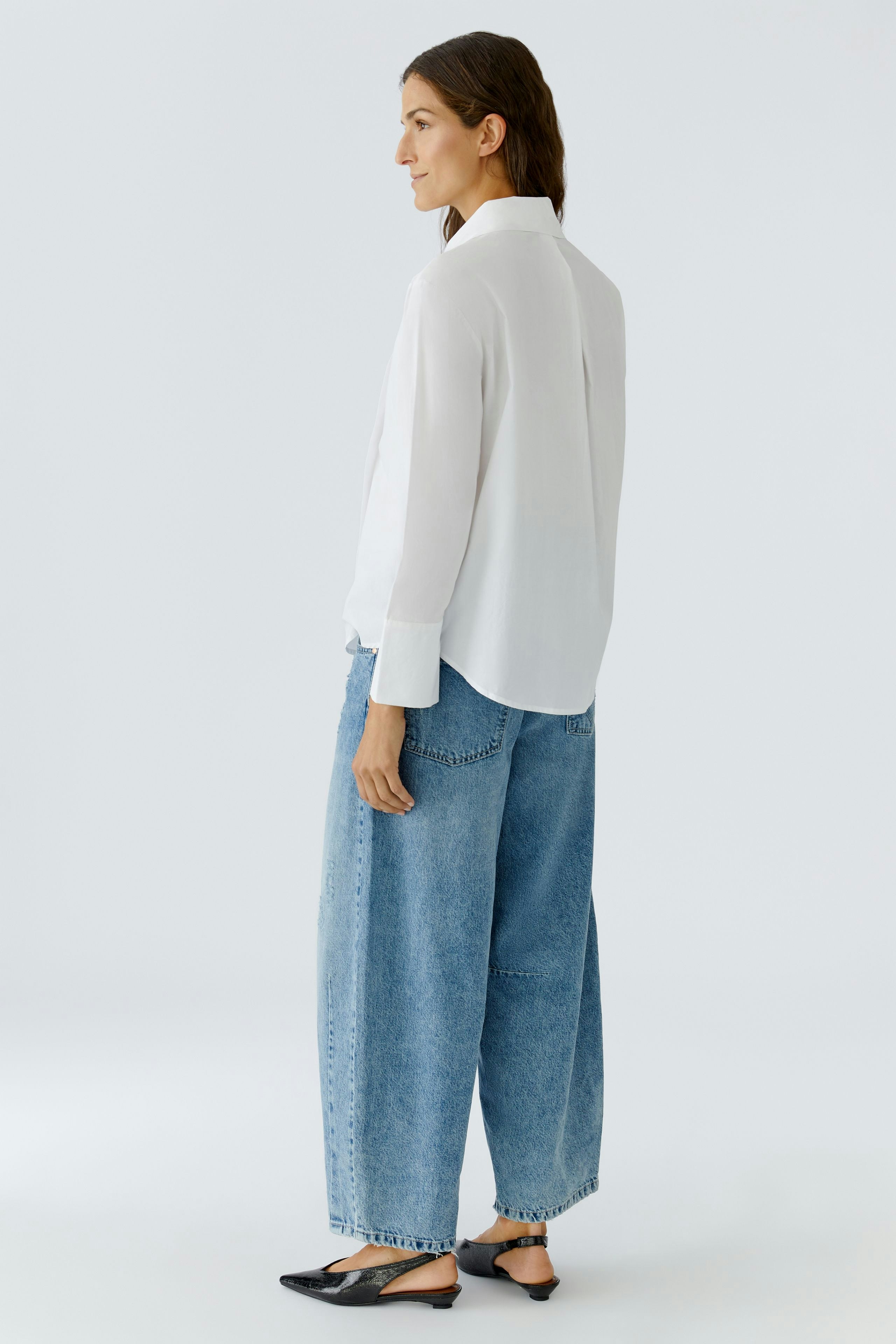 Casual women's blouse: A woman in a white blouse paired with loose denim pants, showcasing a relaxed style.