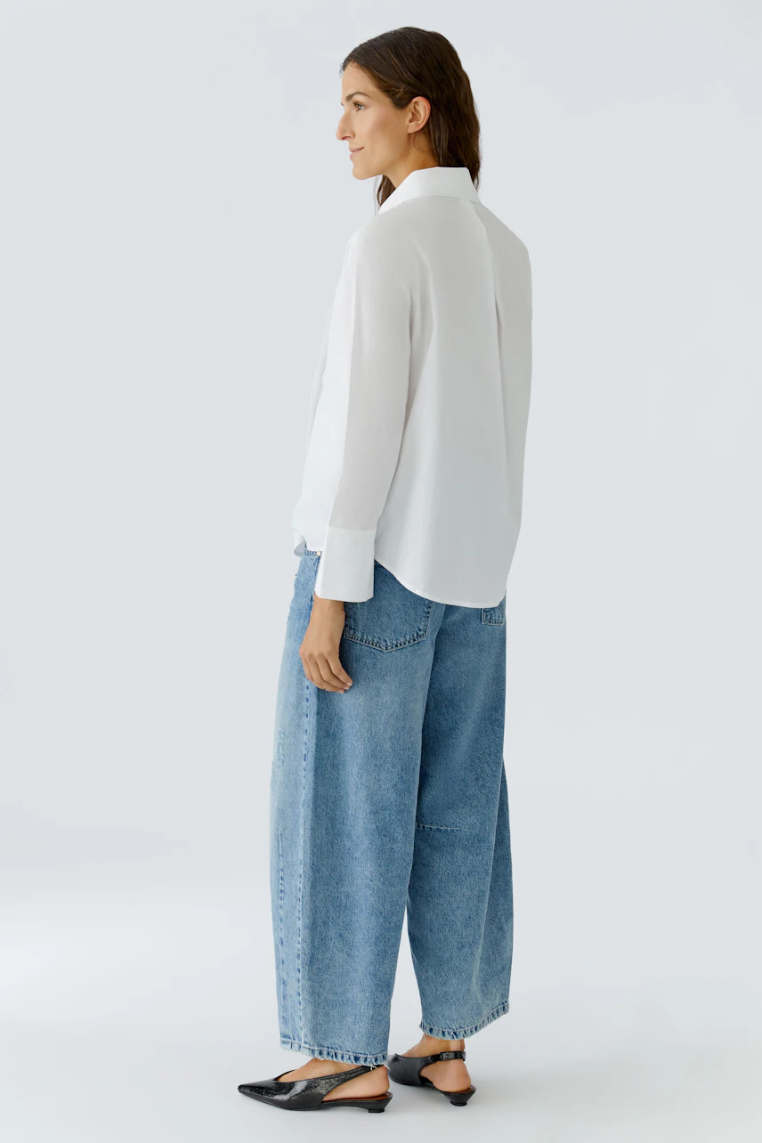 Casual women's blouse: A woman in a white blouse paired with loose denim pants, showcasing a relaxed style.