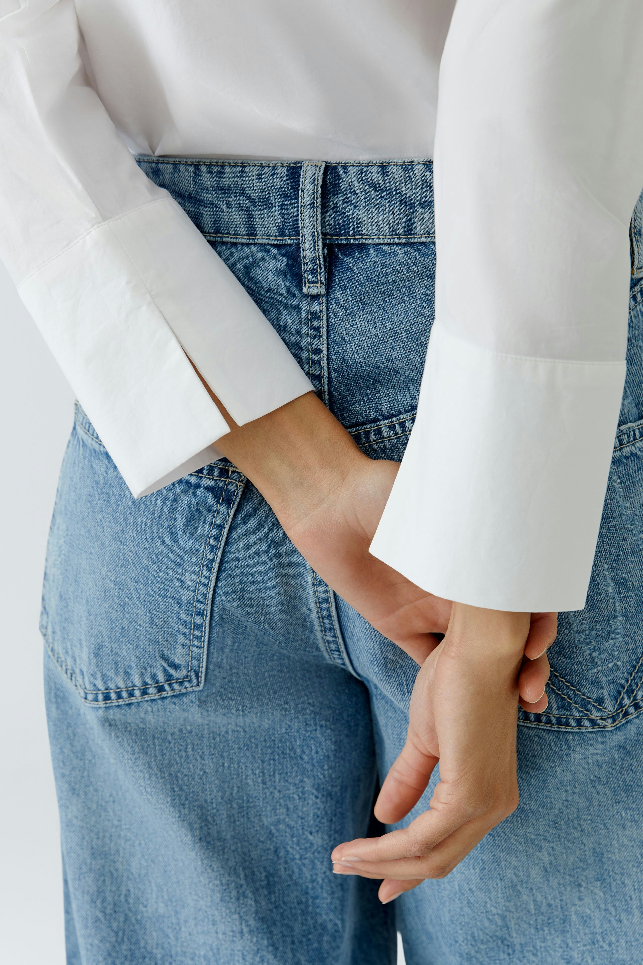 Casual women's blouse: A woman in a white blouse with stylish cuffs, hands behind her back.