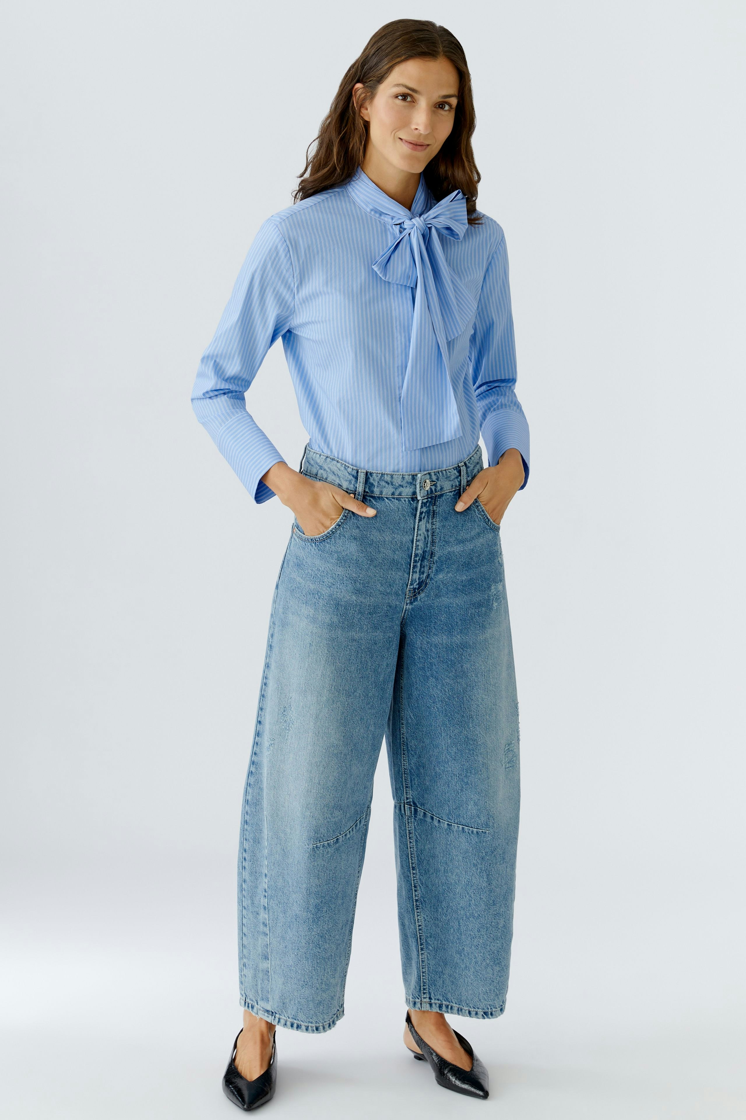 Stylish women's blouse: Woman in a light blue striped blouse with a bow, paired with wide jeans.