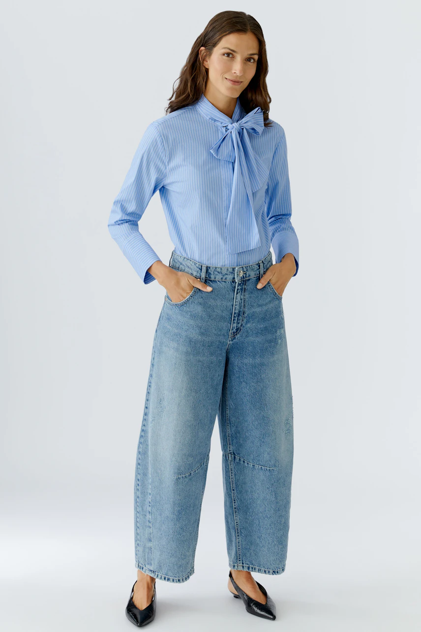 Stylish women's blouse: Woman in a light blue striped blouse with a bow, paired with wide jeans.