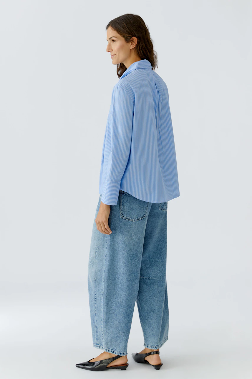 Casual women's blouse: Woman in a light blue striped blouse paired with relaxed-fit jeans.